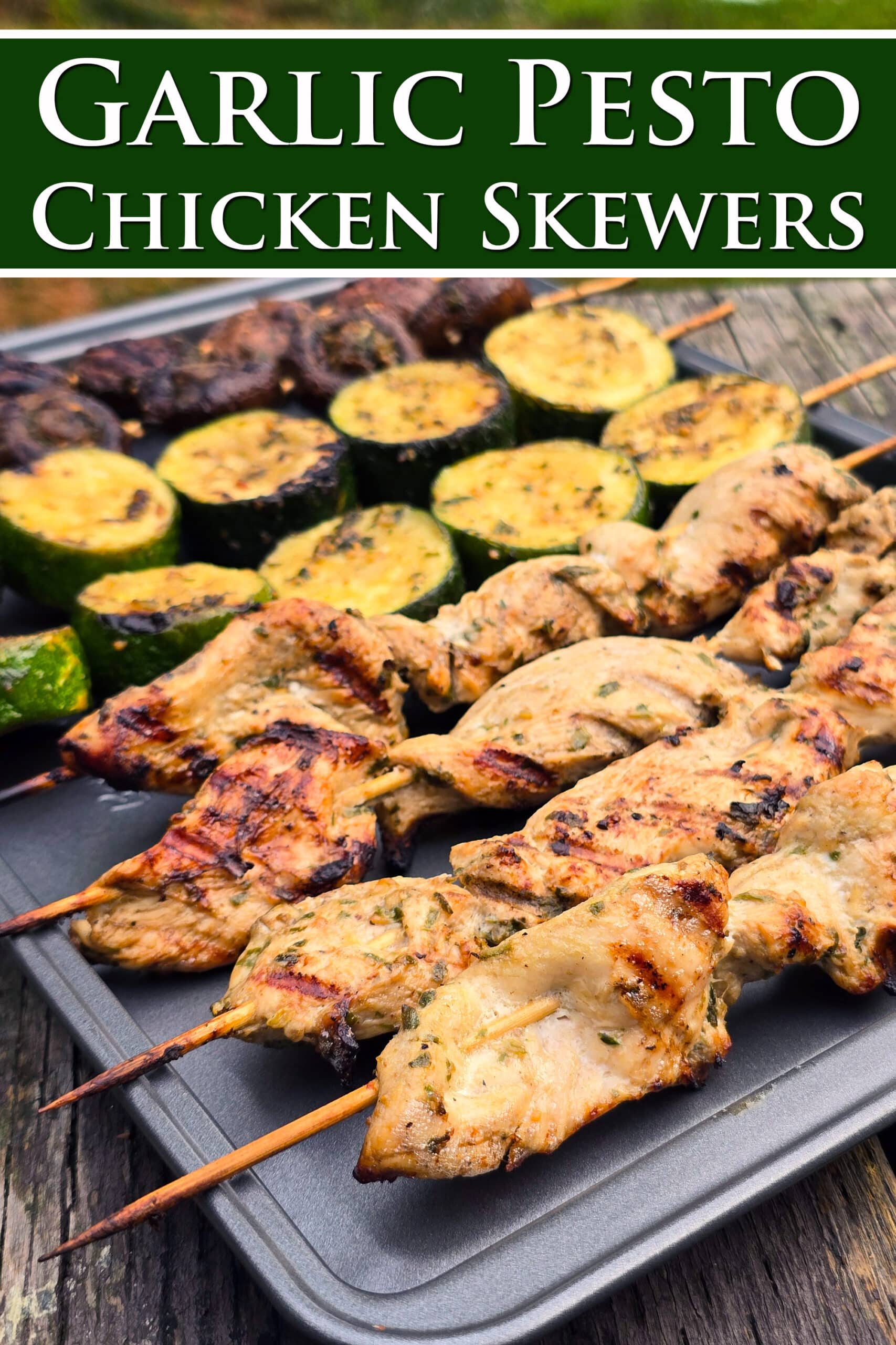 Individual skewers of pesto mushrooms and zucchini slices on a pan with pesto chicken kebabs. Overlaid text says garlic pesto chicken skewers.