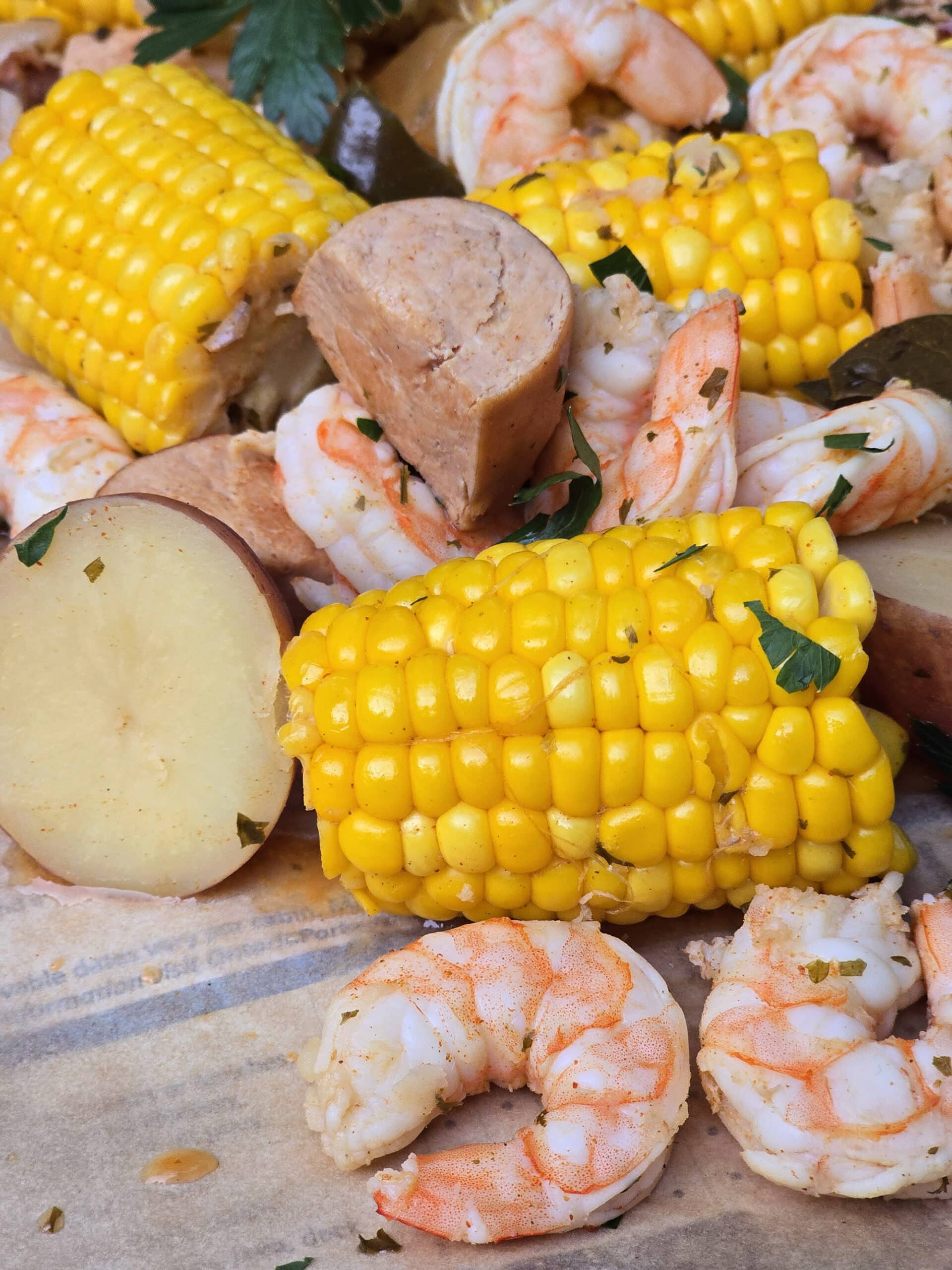 A seafood boil with seasoned shrimp, corn, potatoes, and sausage, on parchment.