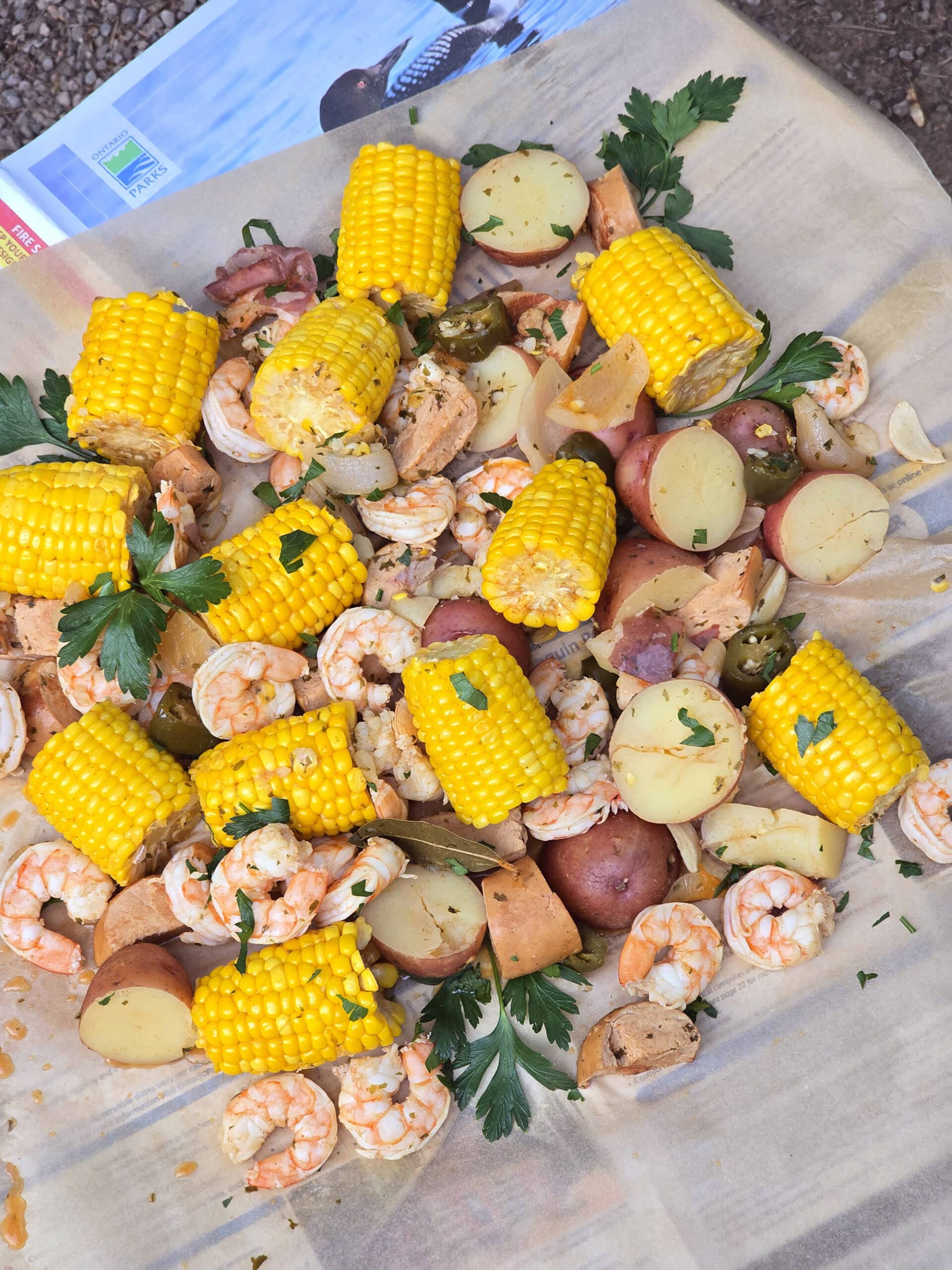 A shrimp boil with seasoned shrimp, corn, potatoes, and sausage, on parchment.