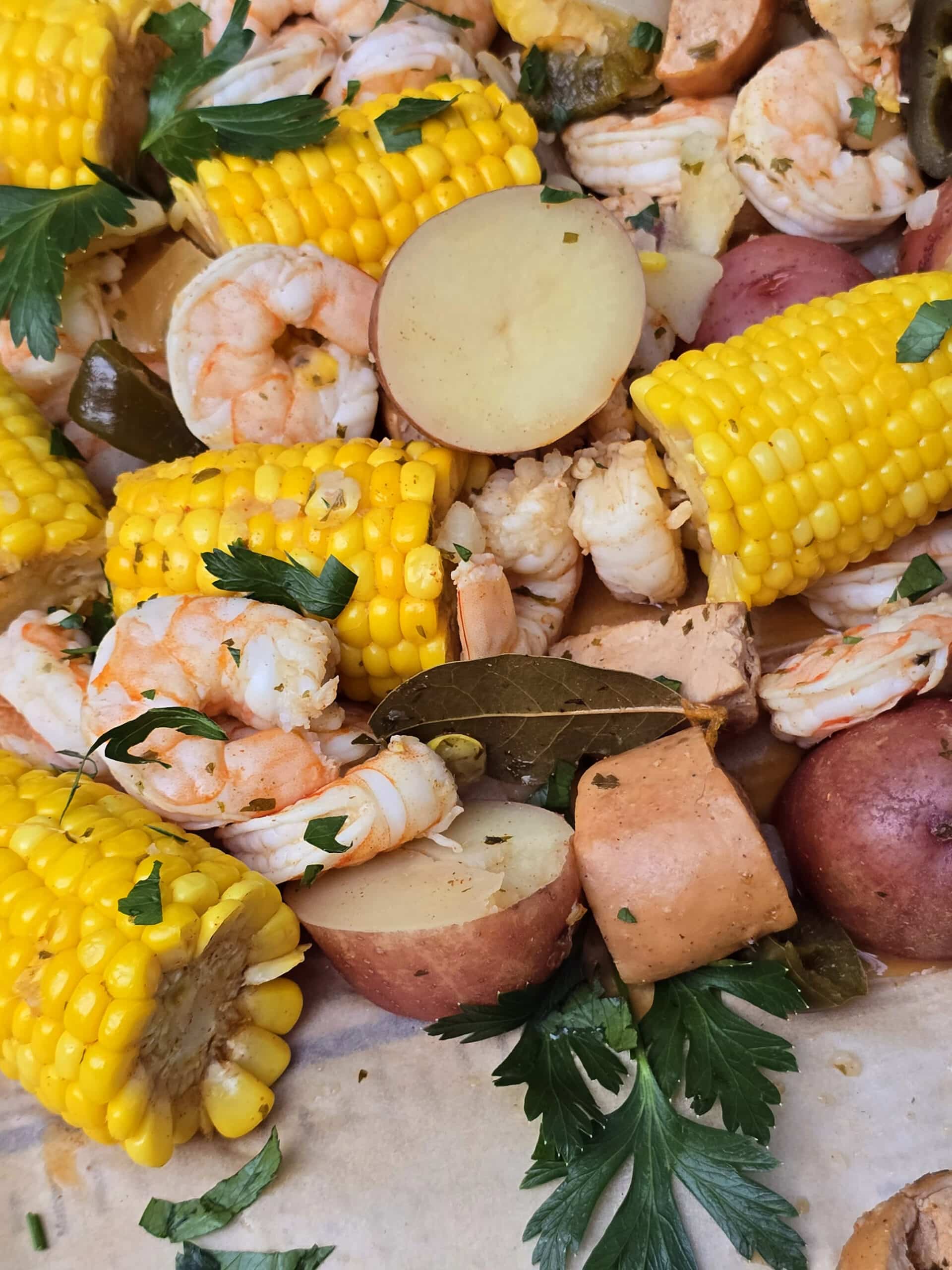 A shrimp boil with seasoned shrimp, corn, potatoes, and sausage, on parchment.