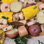 A shrimp boil with seasoned shrimp, corn, potatoes, and sausage, on parchment.