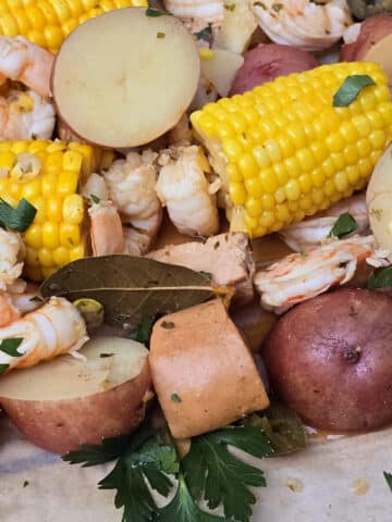 A shrimp boil with seasoned shrimp, corn, potatoes, and sausage, on parchment.