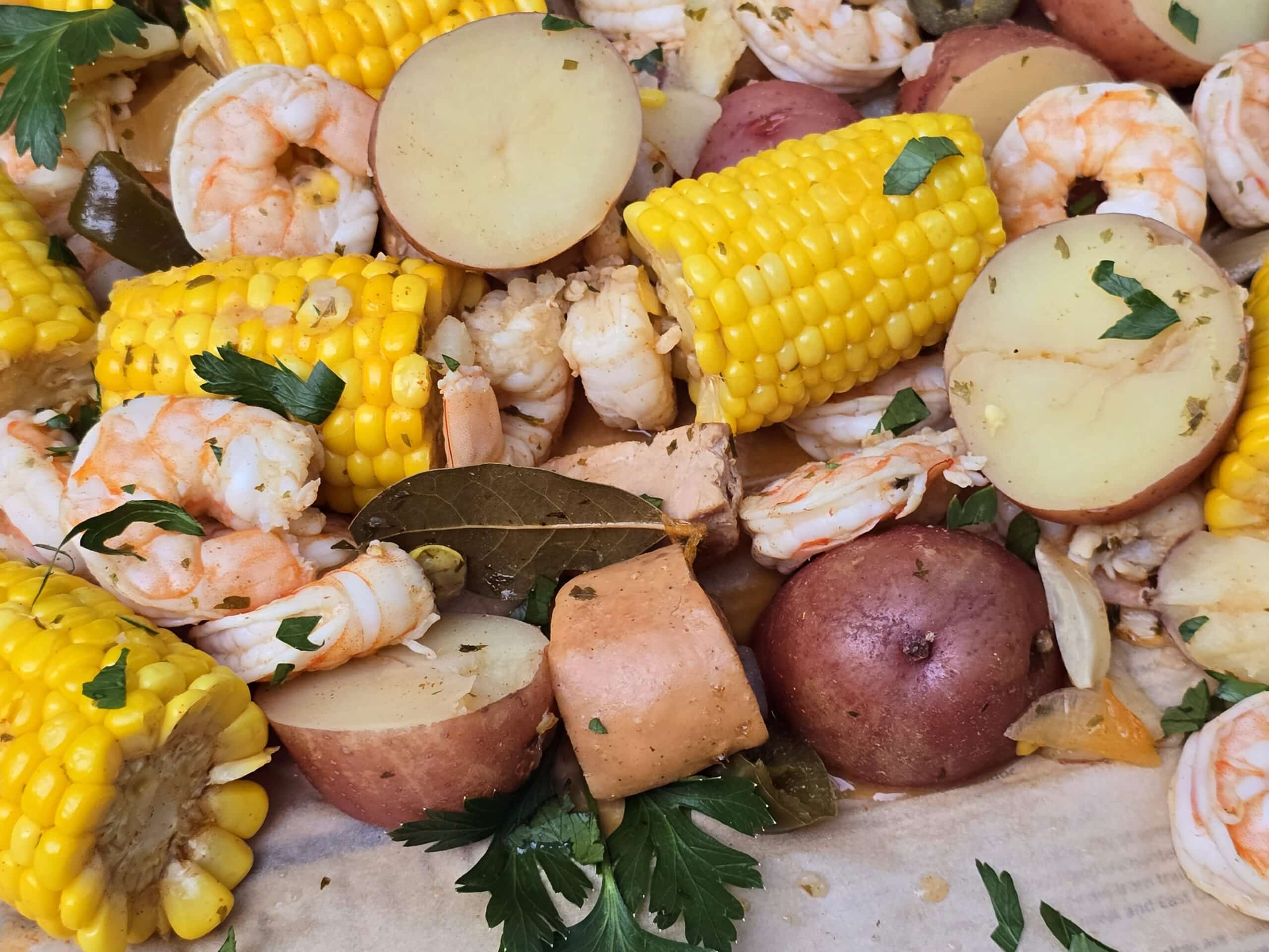 A shrimp boil with seasoned shrimp, corn, potatoes, and sausage, on parchment.