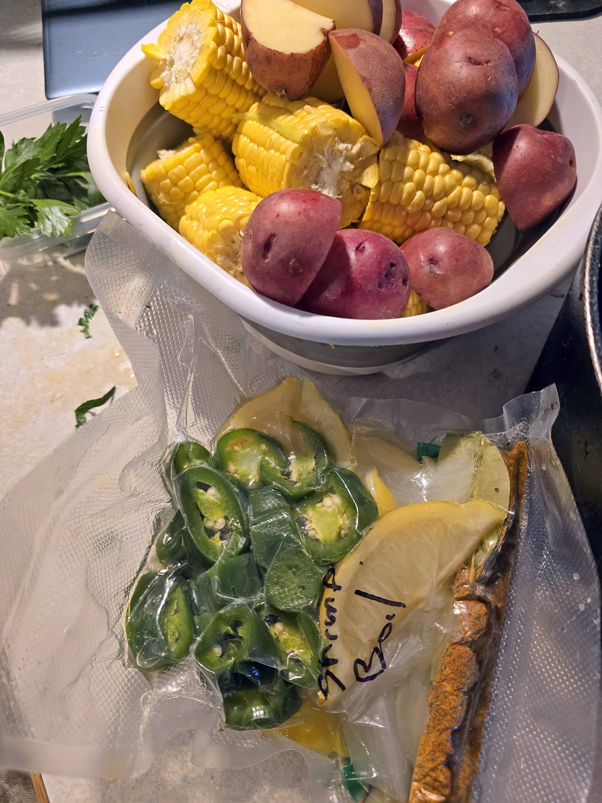 A Large bowl of corn and potatoes, next to a baggie of frozen aromatic ingredients.