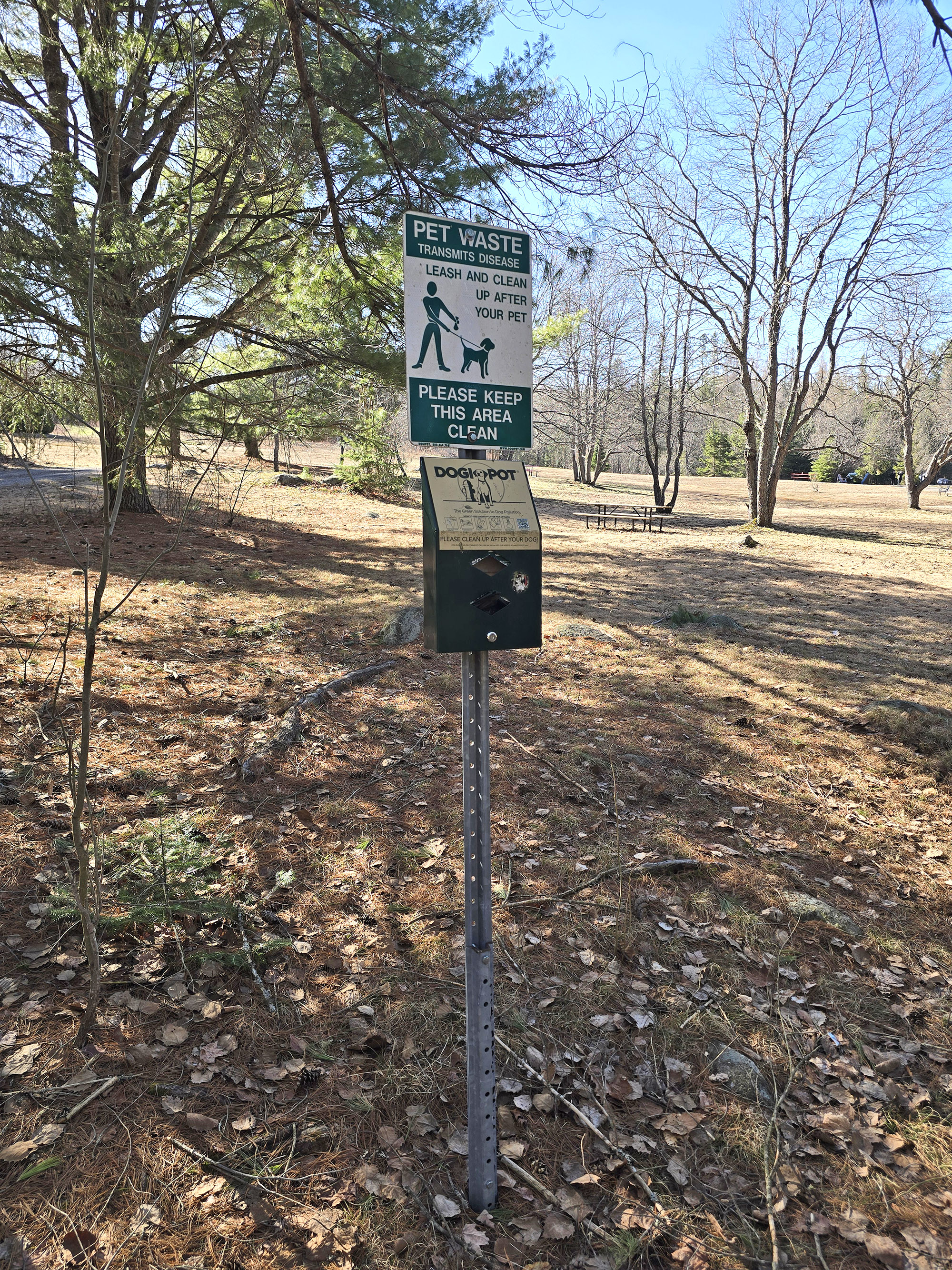 A post with a sign about keeping dogs leashed, and a doggie poop bag dispenser.