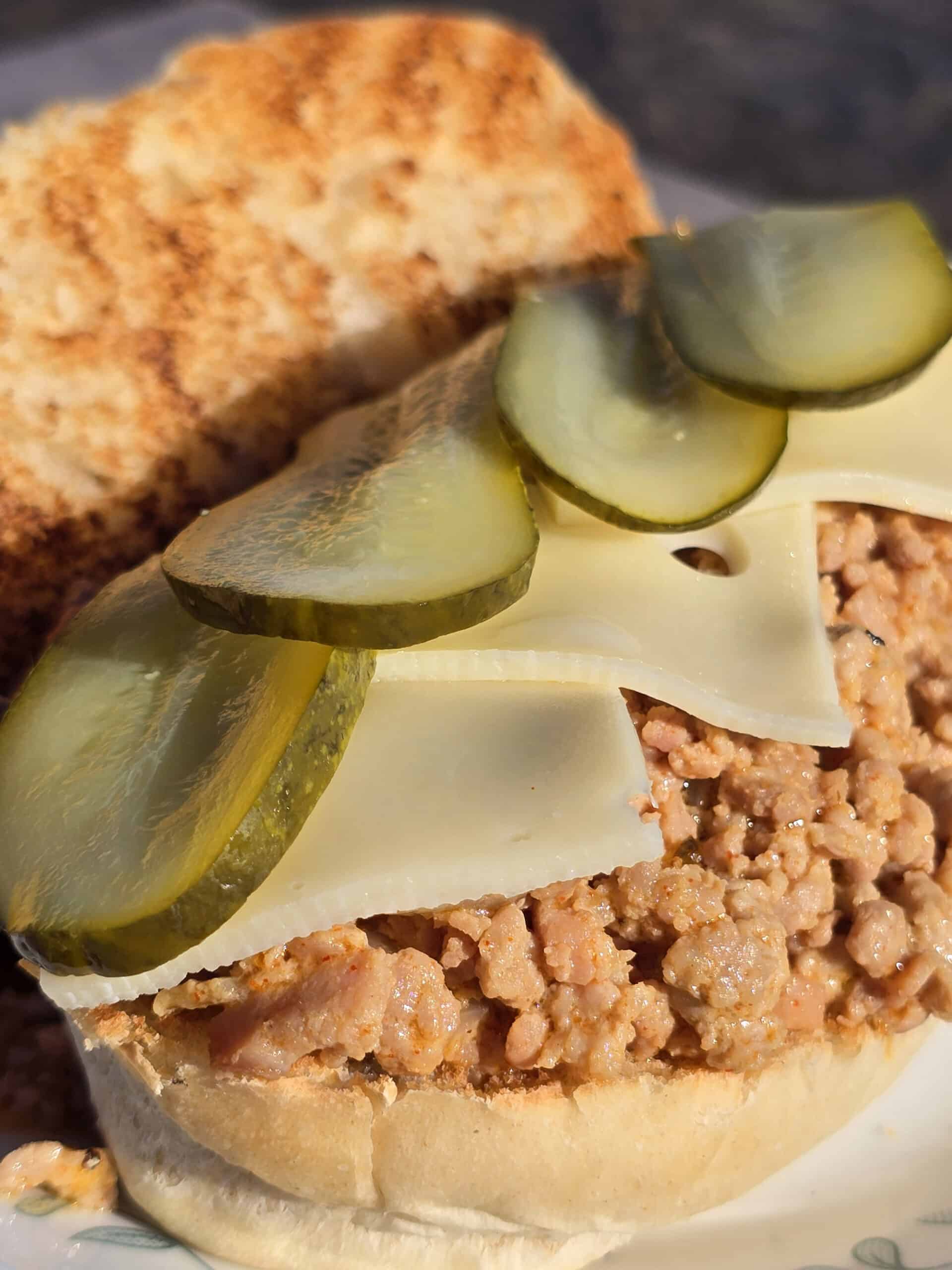 A Cubano Sloppy Joes sandwich with swiss cheese and pickles on top.