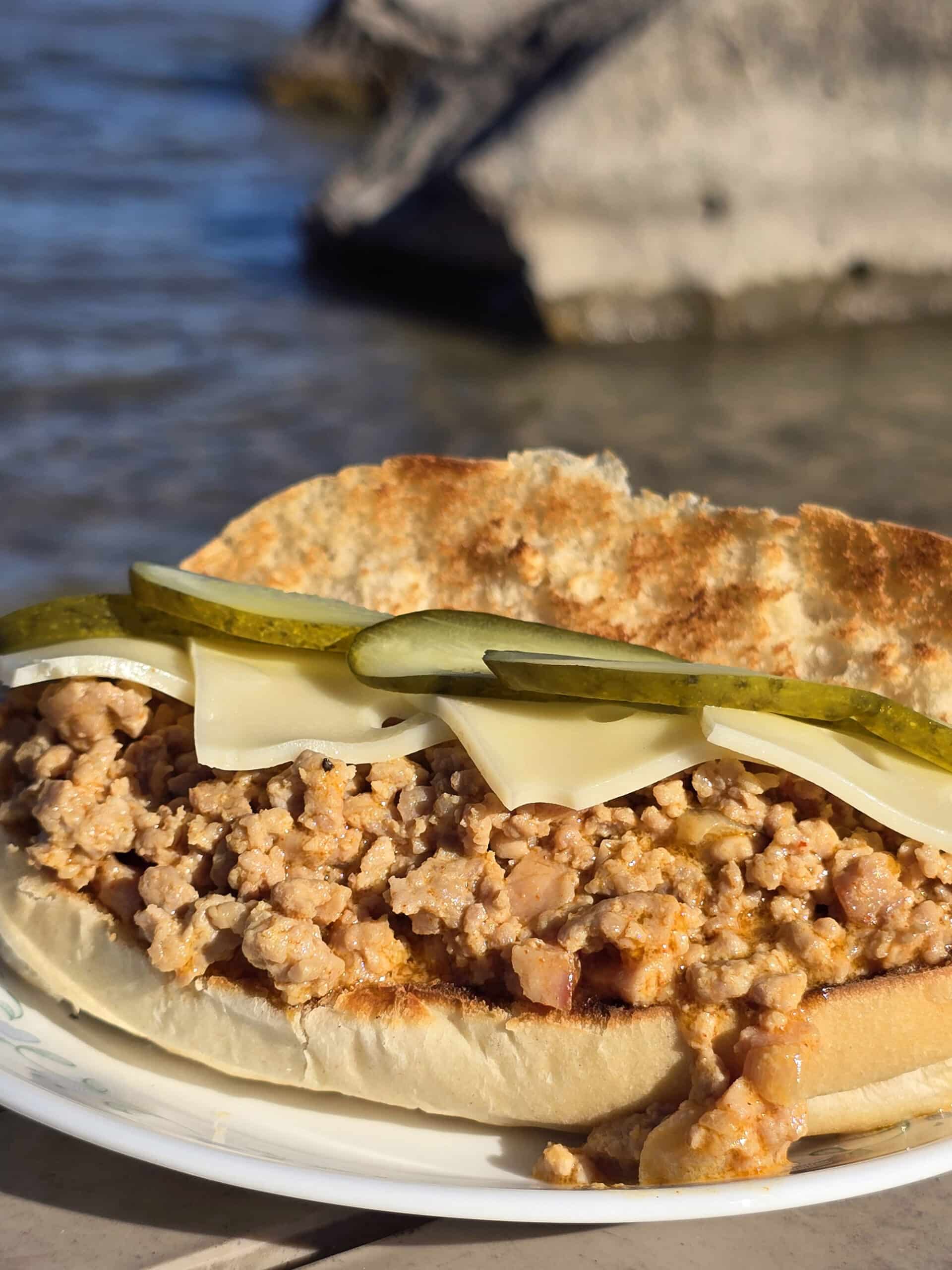 A Cubano Sloppy Joes sandwich with swiss cheese and pickles on top.