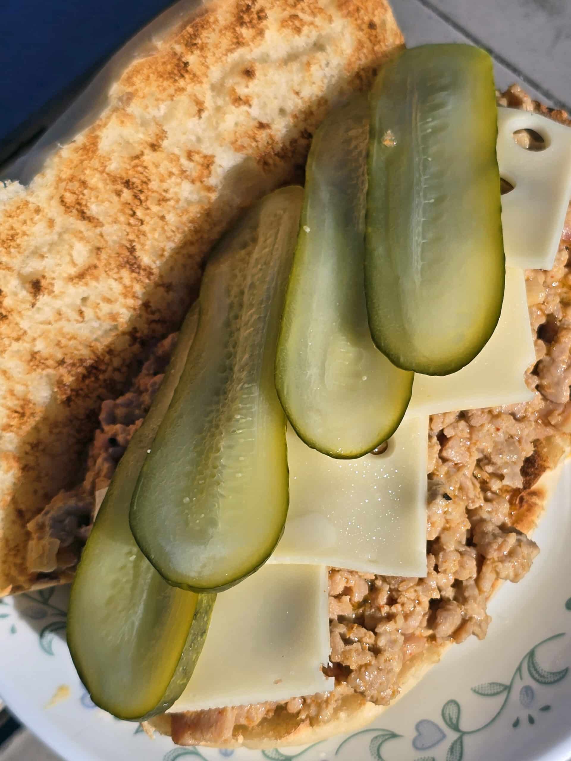 A Cuban Sloppy Joes sandwich with swiss cheese and pickles on top.