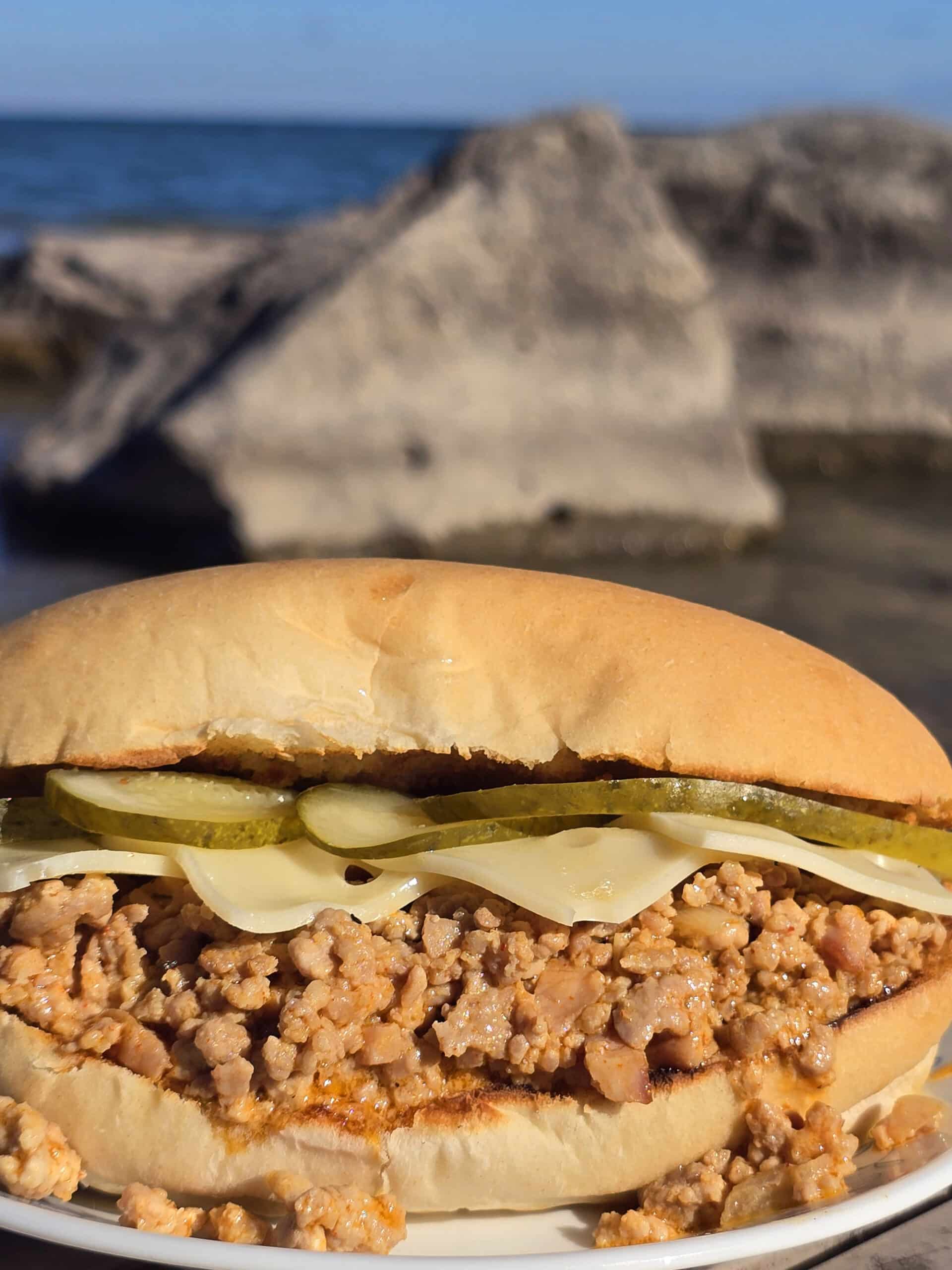 A Cubano Sloppy Joes sandwich with swiss cheese and pickles on top.