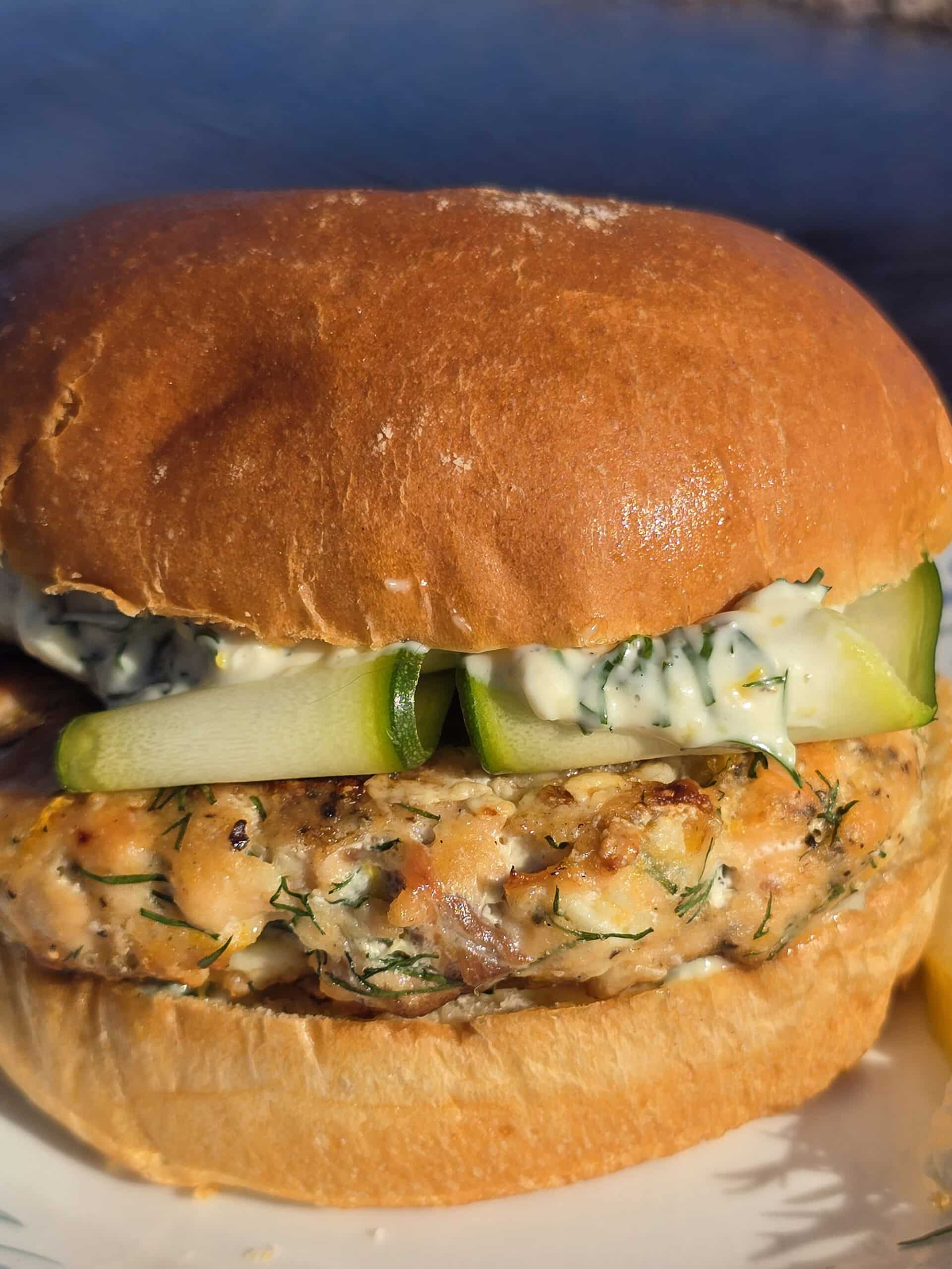 A Mediterranean salmon burger with lemon, dill, and feta in it, and zucchini ribbons on top.