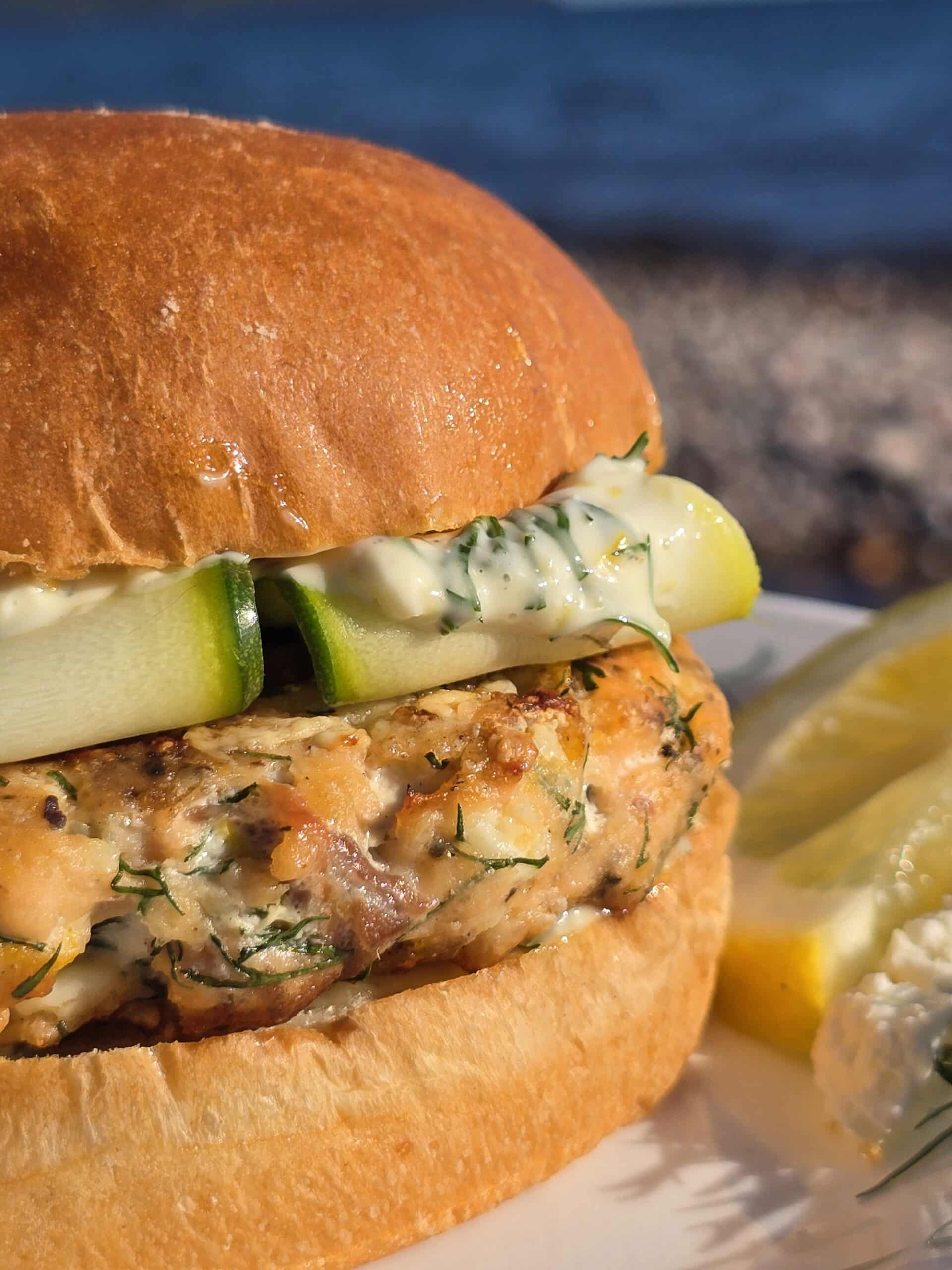 A Mediterranean salmon burger with lemon, dill, and feta in it, and zucchini ribbons on top.