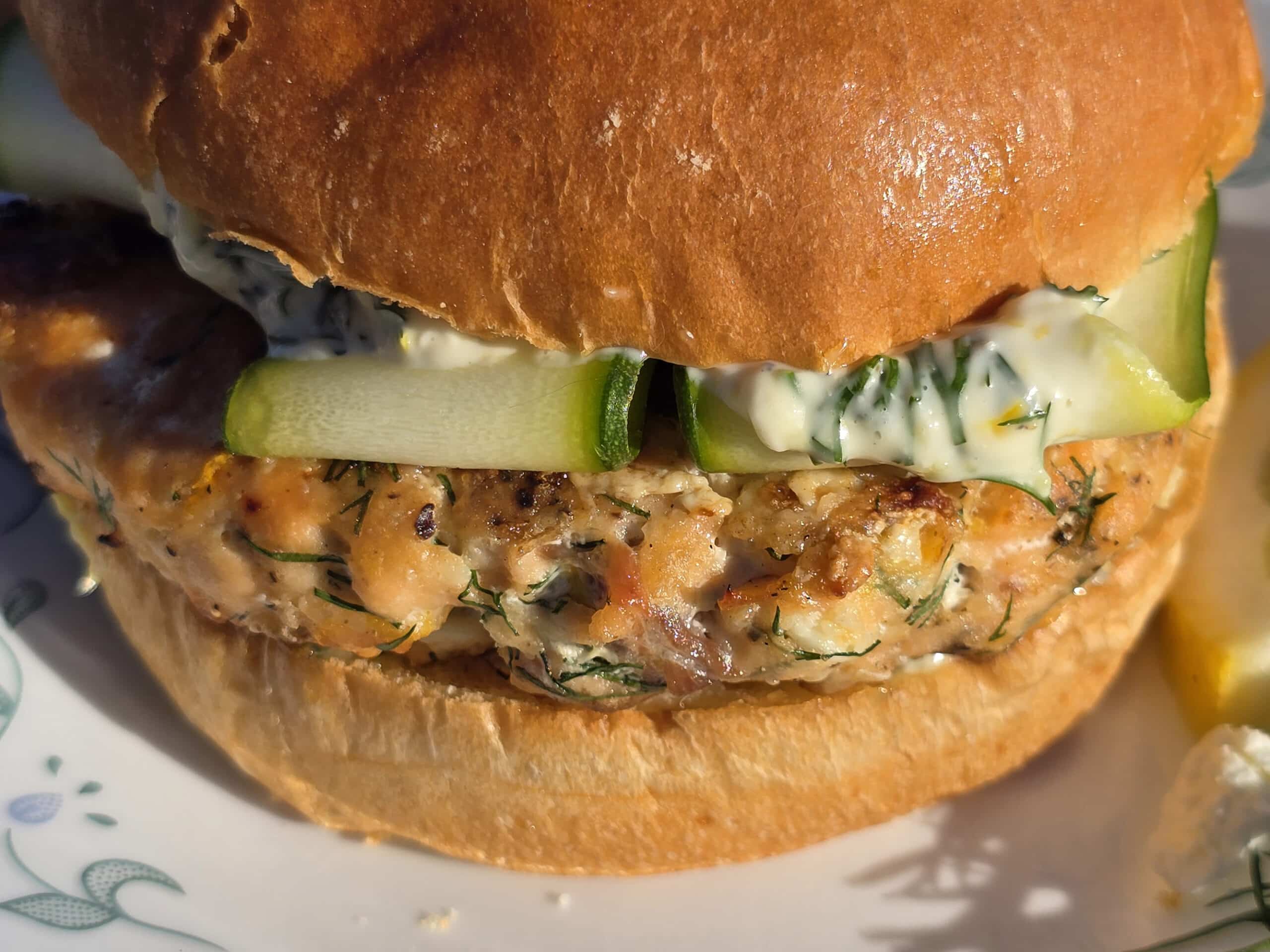 A Mediterranean fresh salmon burger with lemon, dill, and feta in it, and zucchini ribbons on top.