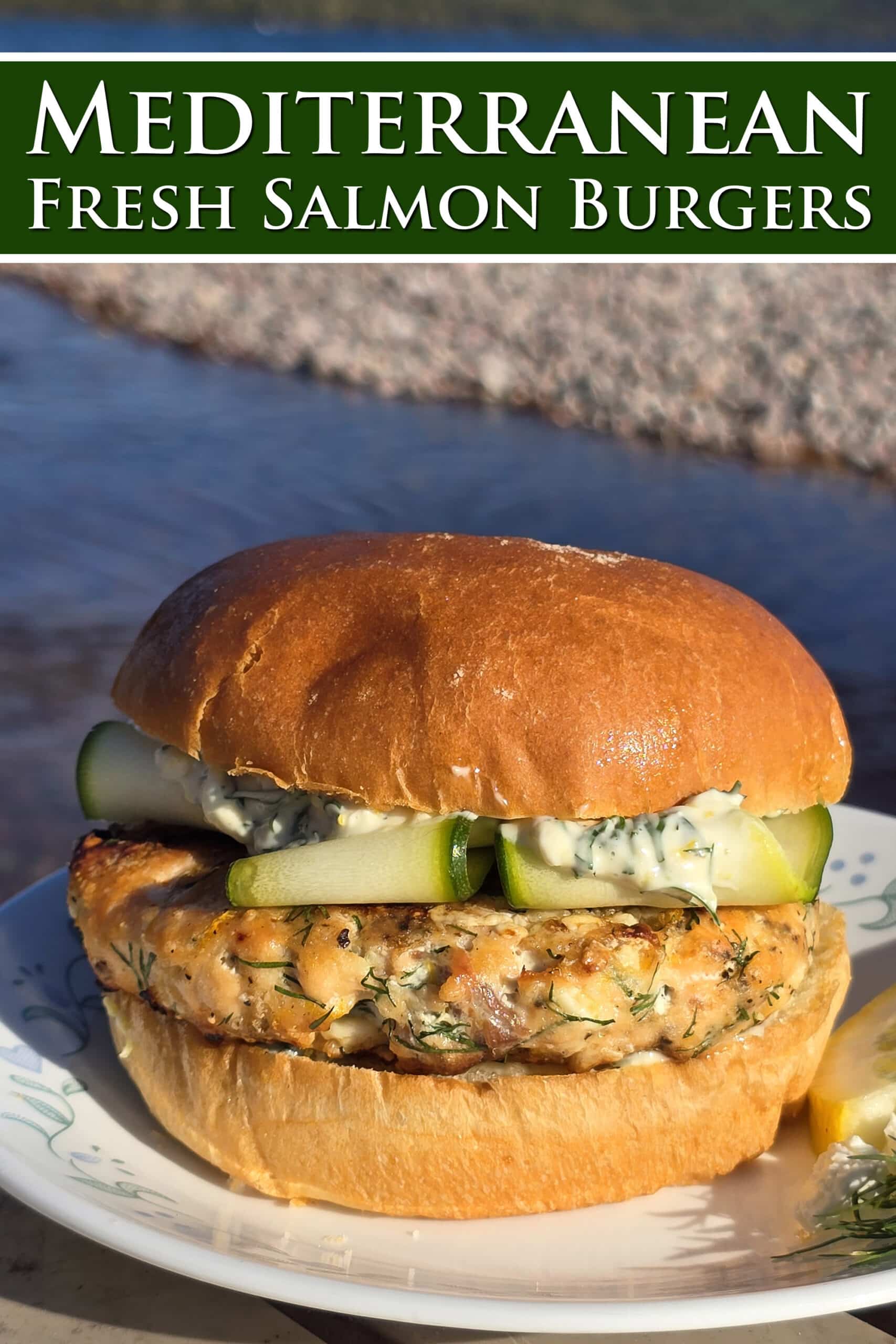 A Mediterranean salmon burger with lemon, dill, and feta in it, and zucchini ribbons on top. Overlaid text says Mediterranean fresh salmon burgers.