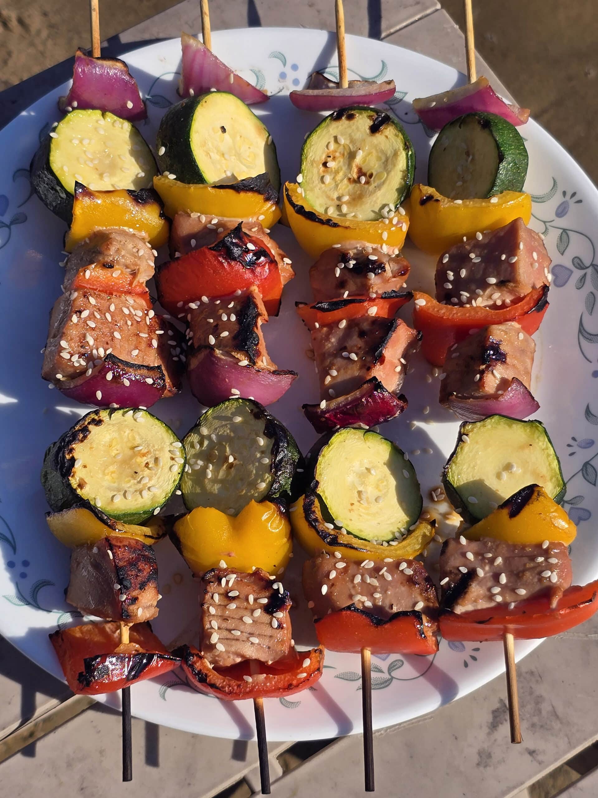 A plate of sesame ginger ahi tuna skewers, with fresh tuna, red and yellow peppers, red onion, and zucchini rounds.