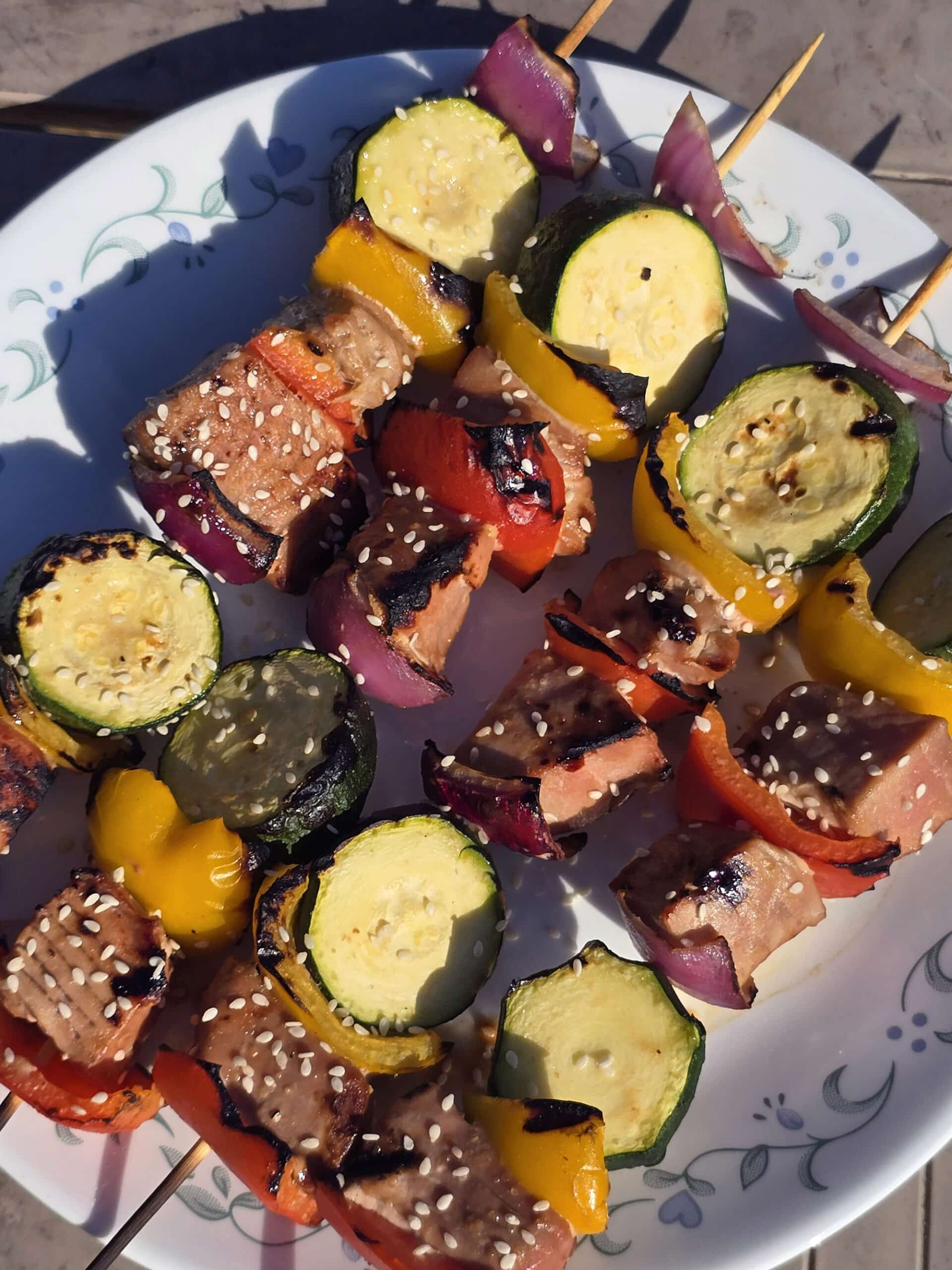 A plate of sesame ginger tuna skewers, with fresh tuna, red and yellow peppers, red onion, and zucchini rounds.