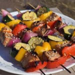 A plate of sesame ginger tuna kebabs, with fresh tuna, red and yellow peppers, red onion, and zucchini rounds.