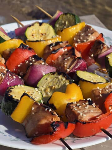 A plate of sesame ginger tuna kebabs, with fresh tuna, red and yellow peppers, red onion, and zucchini rounds.