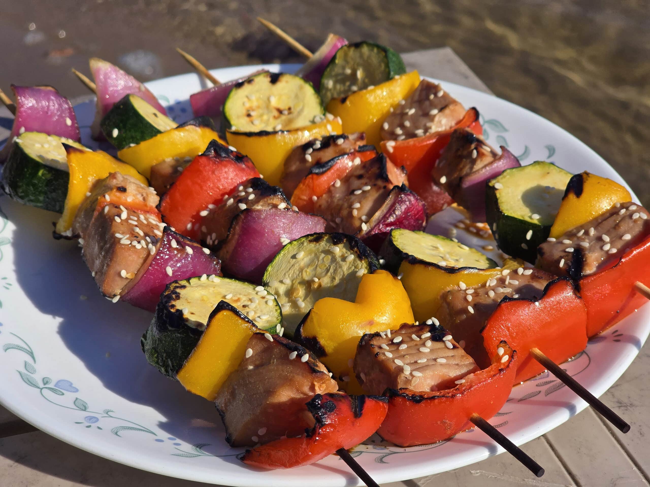 A plate of sesame ginger tuna kebabs, with fresh tuna, red and yellow peppers, red onion, and zucchini rounds.