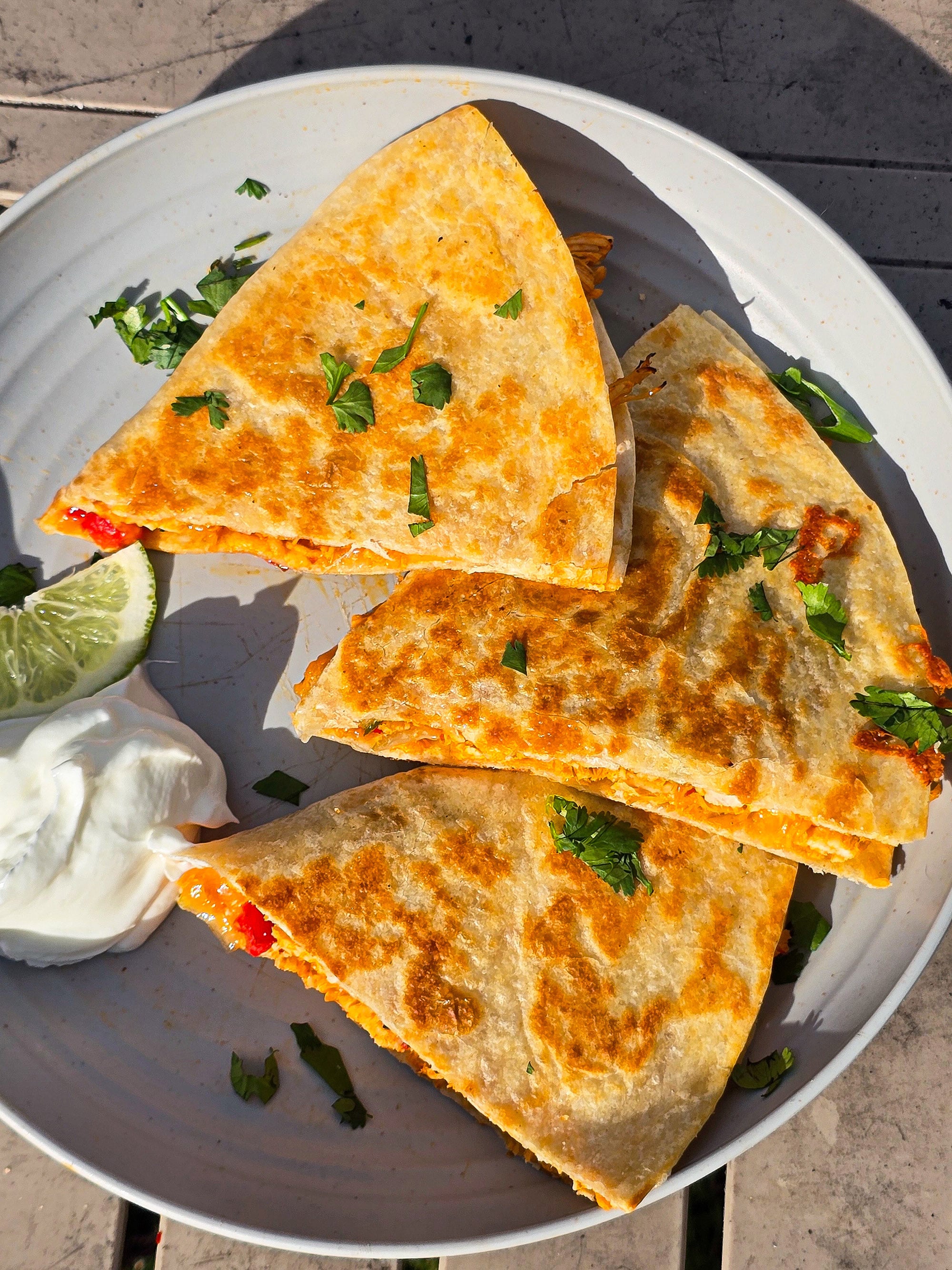 A sliced grilled chicken quesadilla on a plate with sour cream and cilantro.