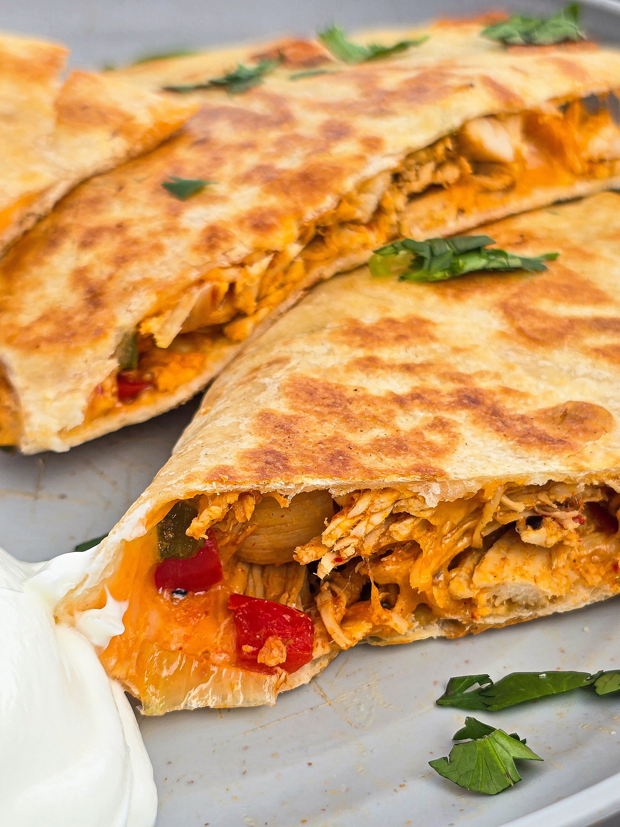 A sliced grilled chicken quesadilla on a plate with sour cream and cilantro.