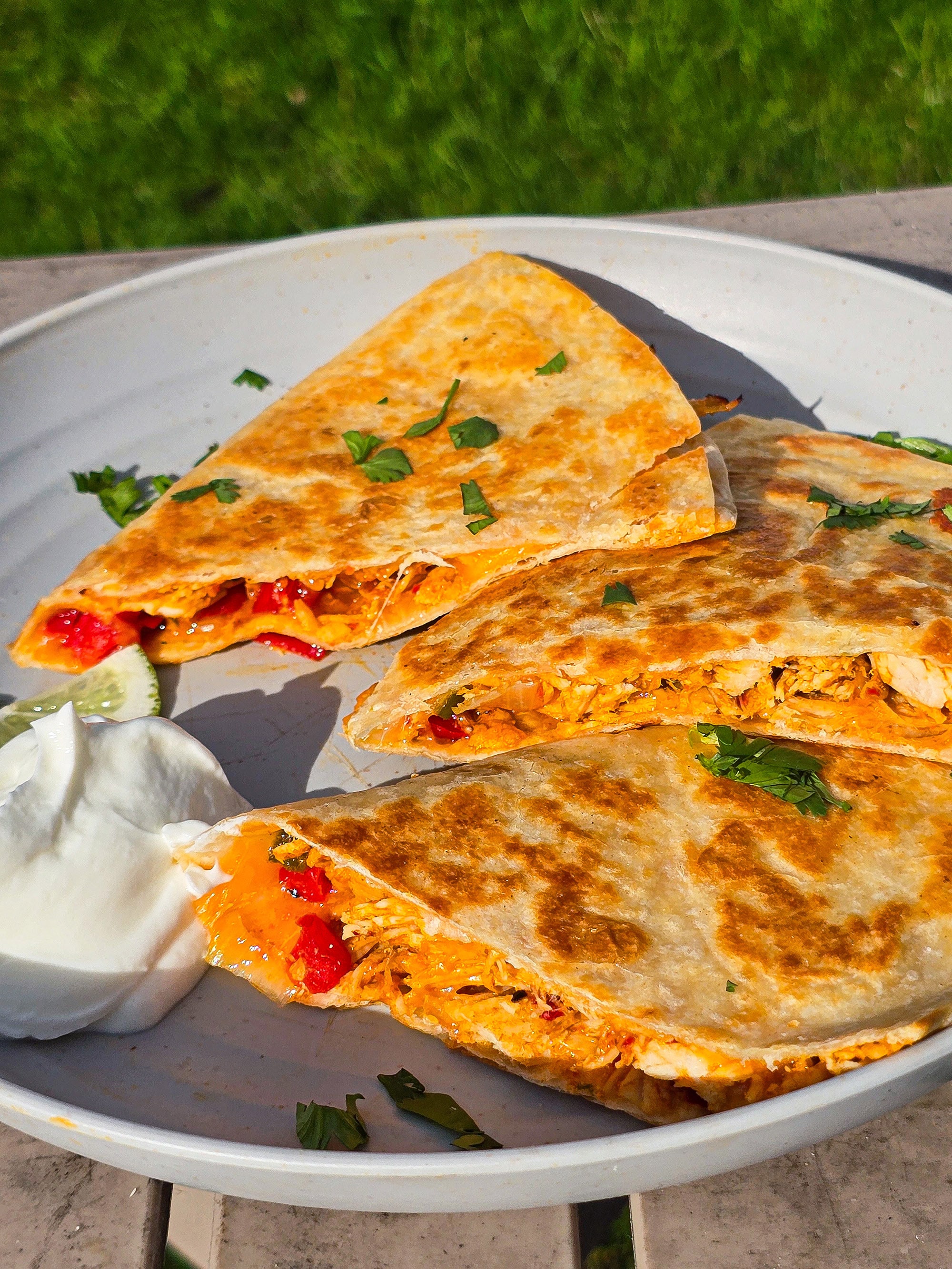Grilled chicken quesadillas on a plate with sour cream and cilantro.