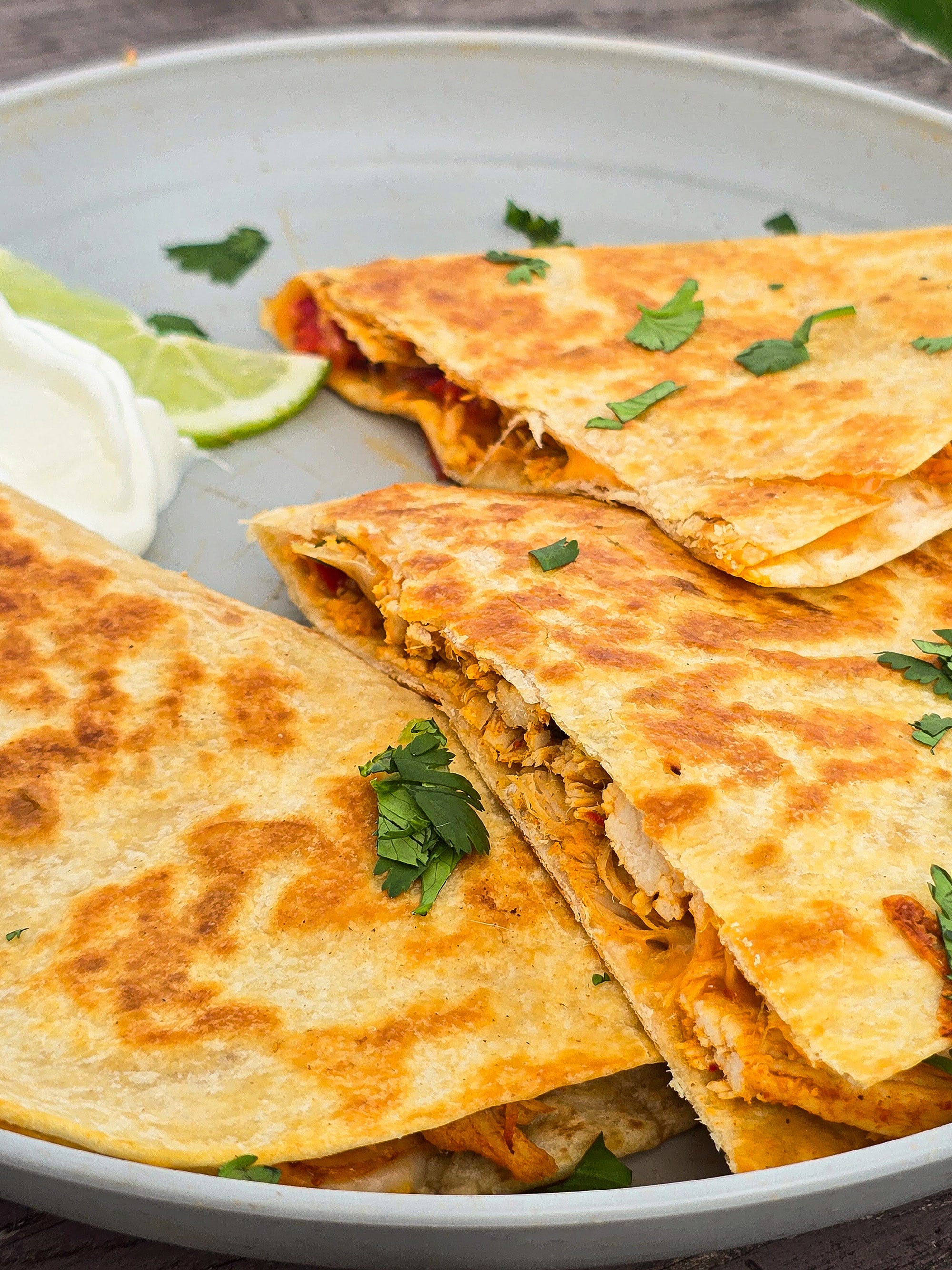 A sliced grilled chicken quesadilla on a plate with sour cream and cilantro.