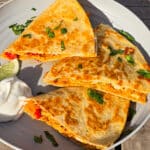 Grilled chicken quesadillas on a plate with sour cream and cilantro.