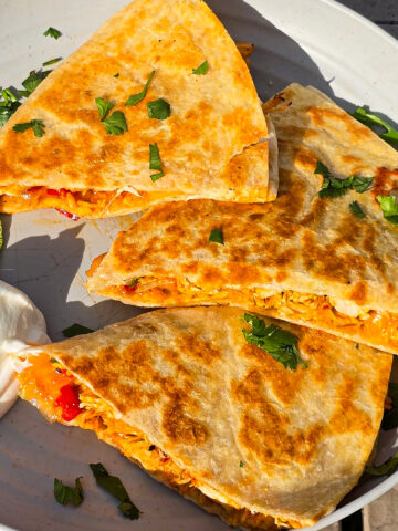 Grilled chicken quesadillas on a plate with sour cream and cilantro.