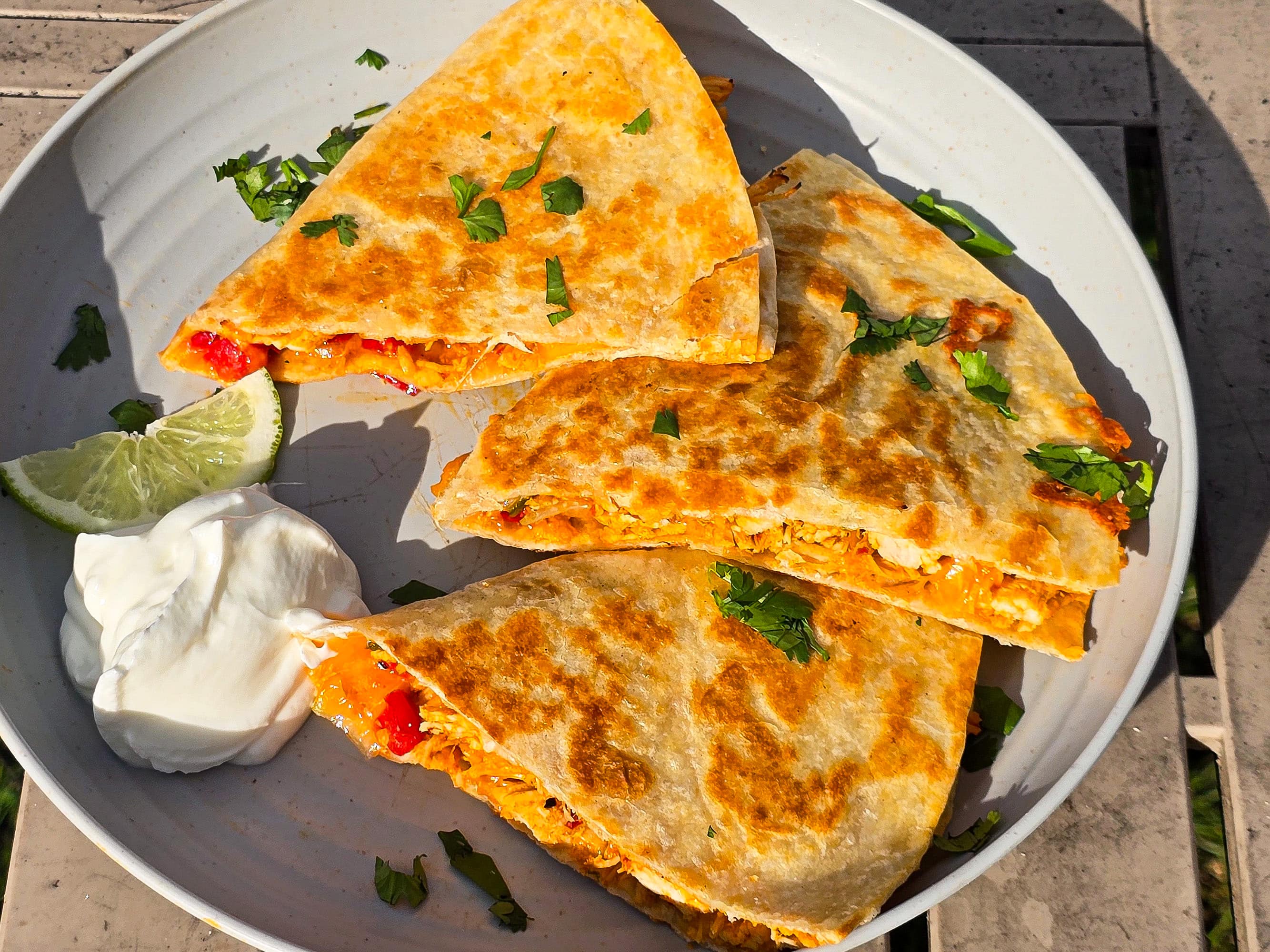 Grilled chicken quesadillas on a plate with sour cream and cilantro.