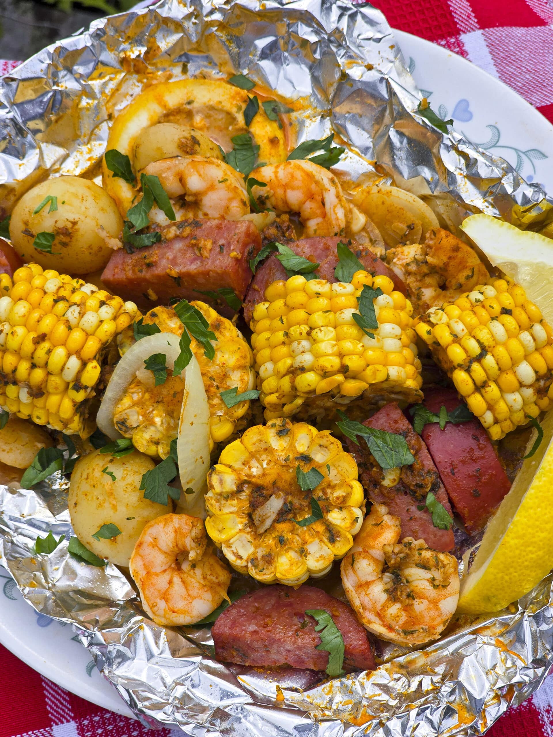 A large serving of seafood boil foil packet meal, on a plate. It has chunks of corn, sausage, potatoes, and shrimp in an obviously heavily seasoned sauce.