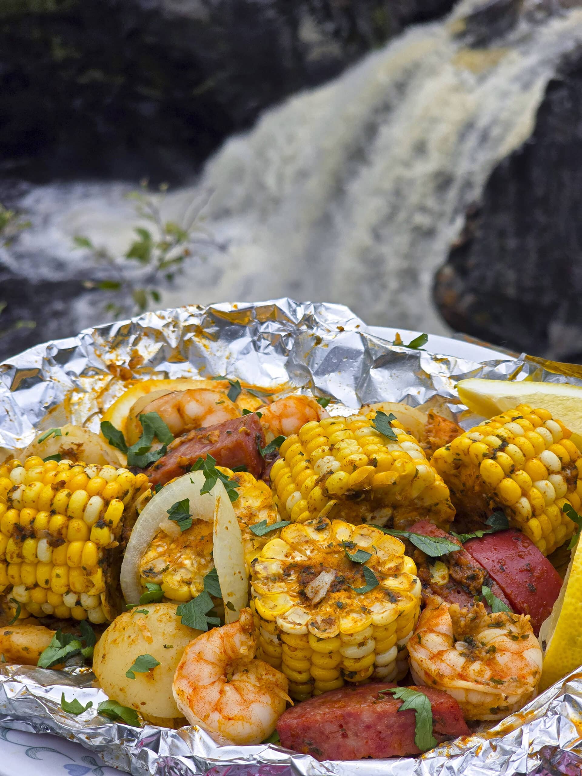 A large serving of shrimp boil foil packet meal, on a plate. It has chunks of corn, sausage, potatoes, and shrimp in an obviously heavily seasoned sauce.