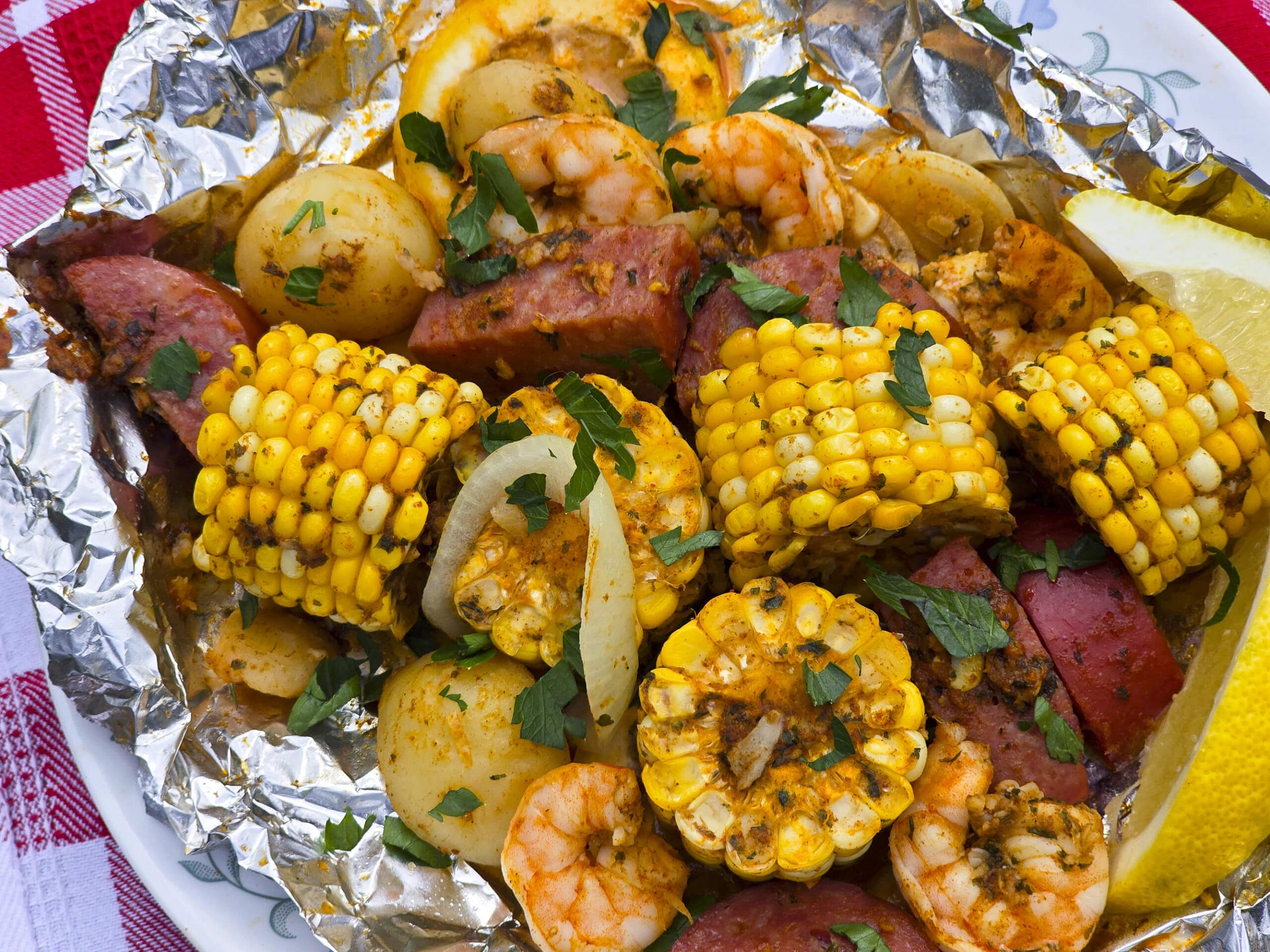A large serving of shrimp boil foil packet meal, on a plate. It has chunks of corn, sausage, potatoes, and shrimp in an obviously heavily seasoned sauce.