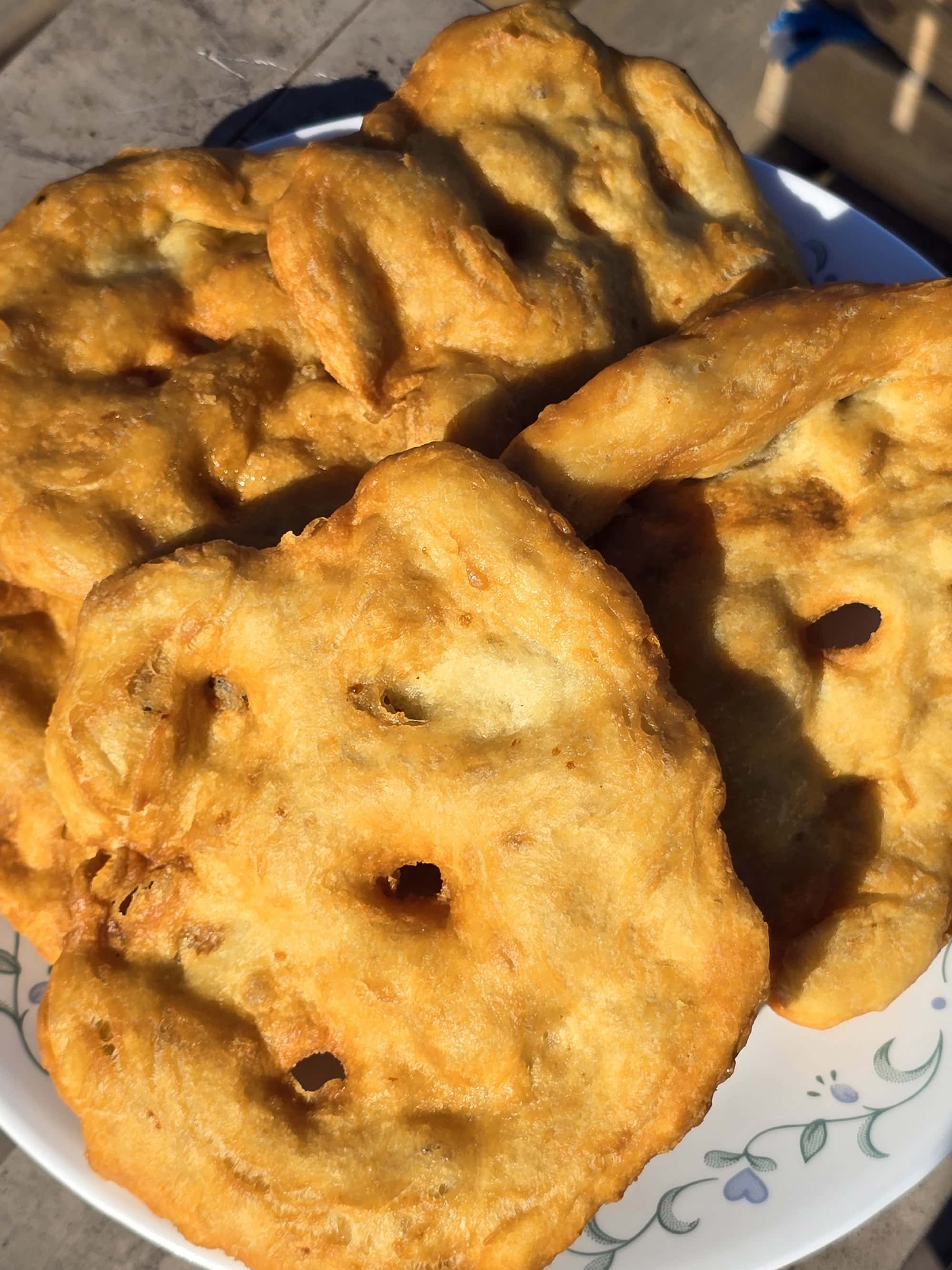 3 large pieces of homemade Fry bread on a plate, on a wooden dock.