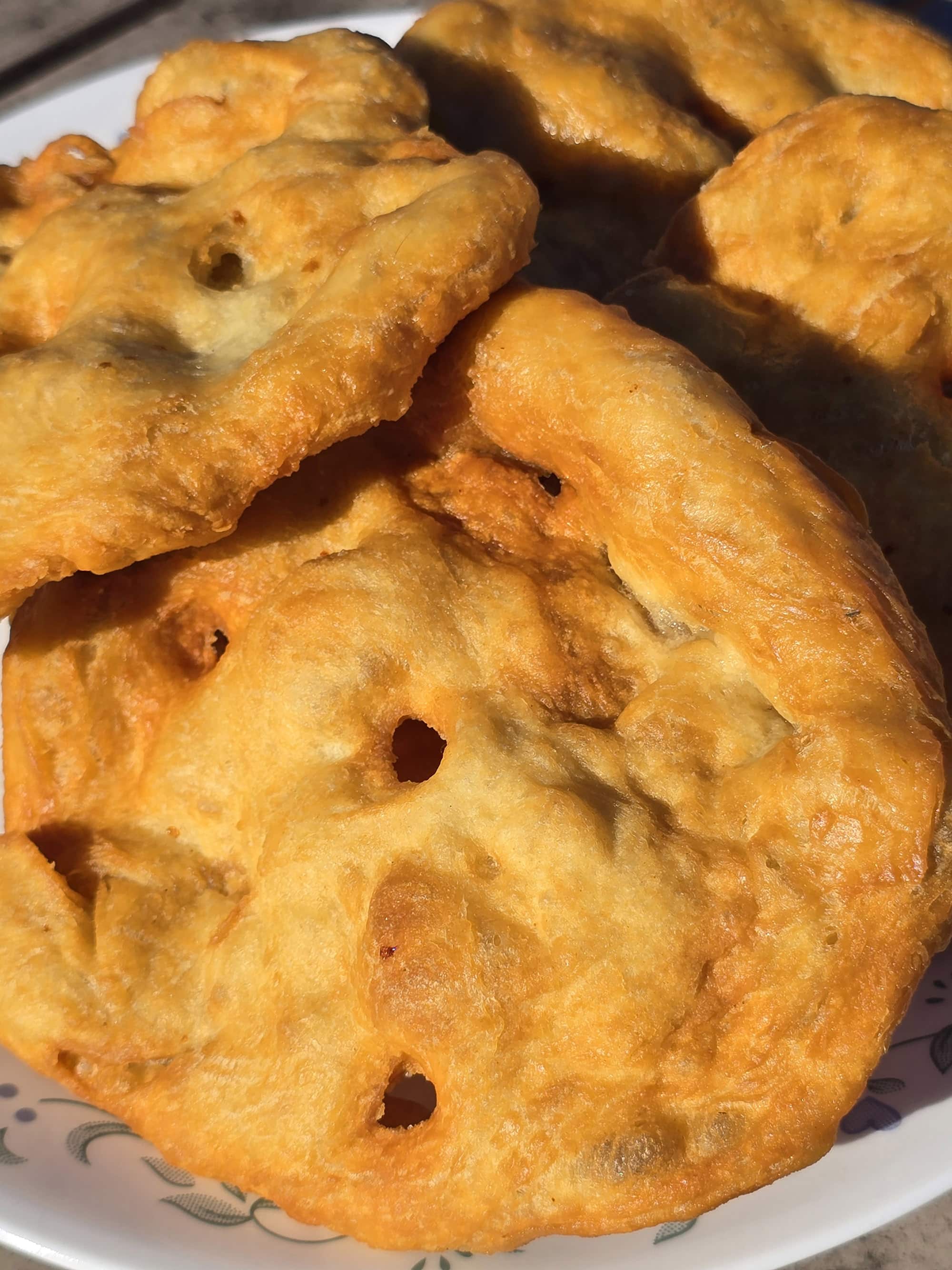 3 large pieces of homemade Frybread on a plate, on a wooden dock.