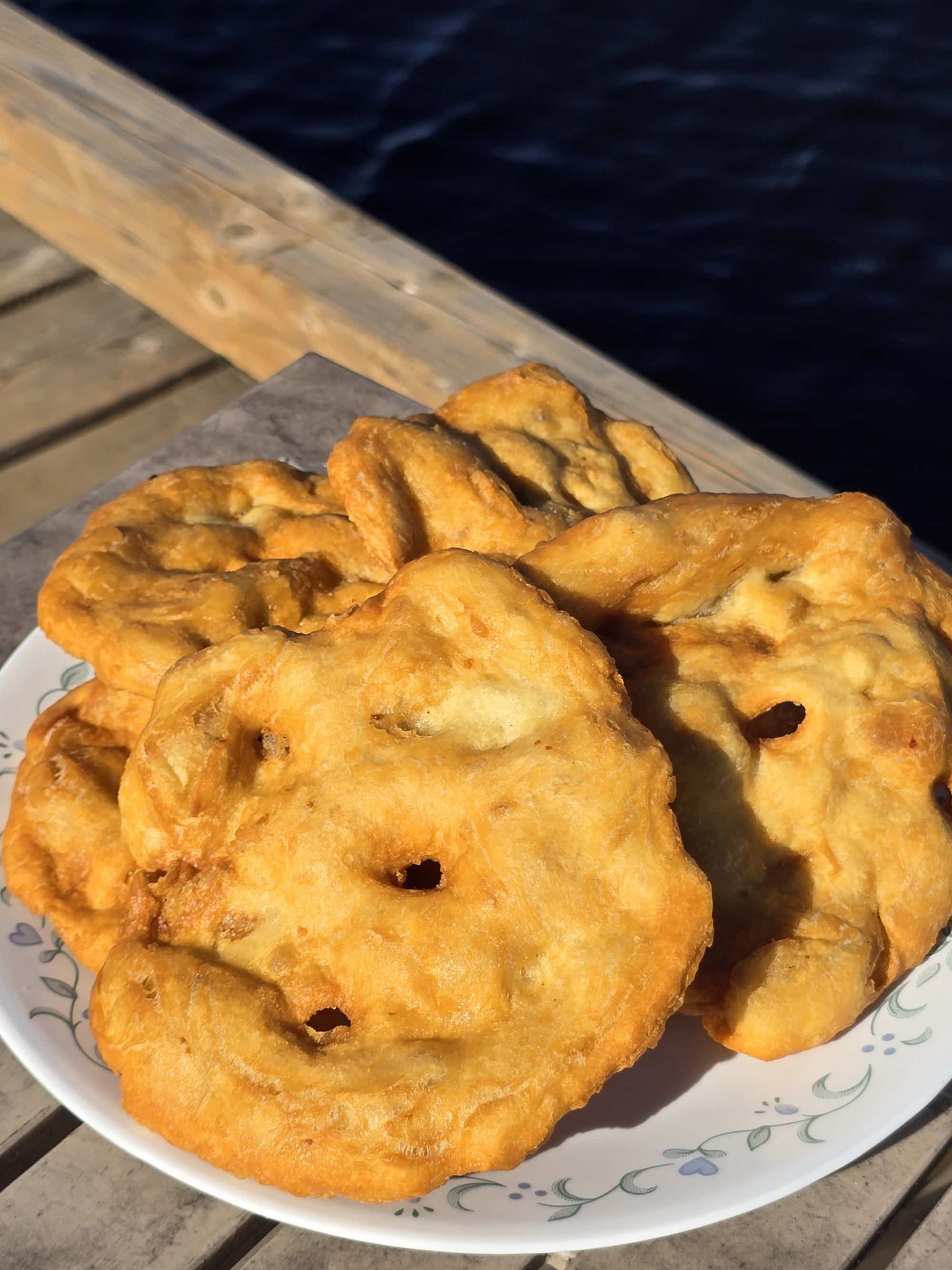 3 large pieces of Indian Frybread on a plate, on a wooden dock.