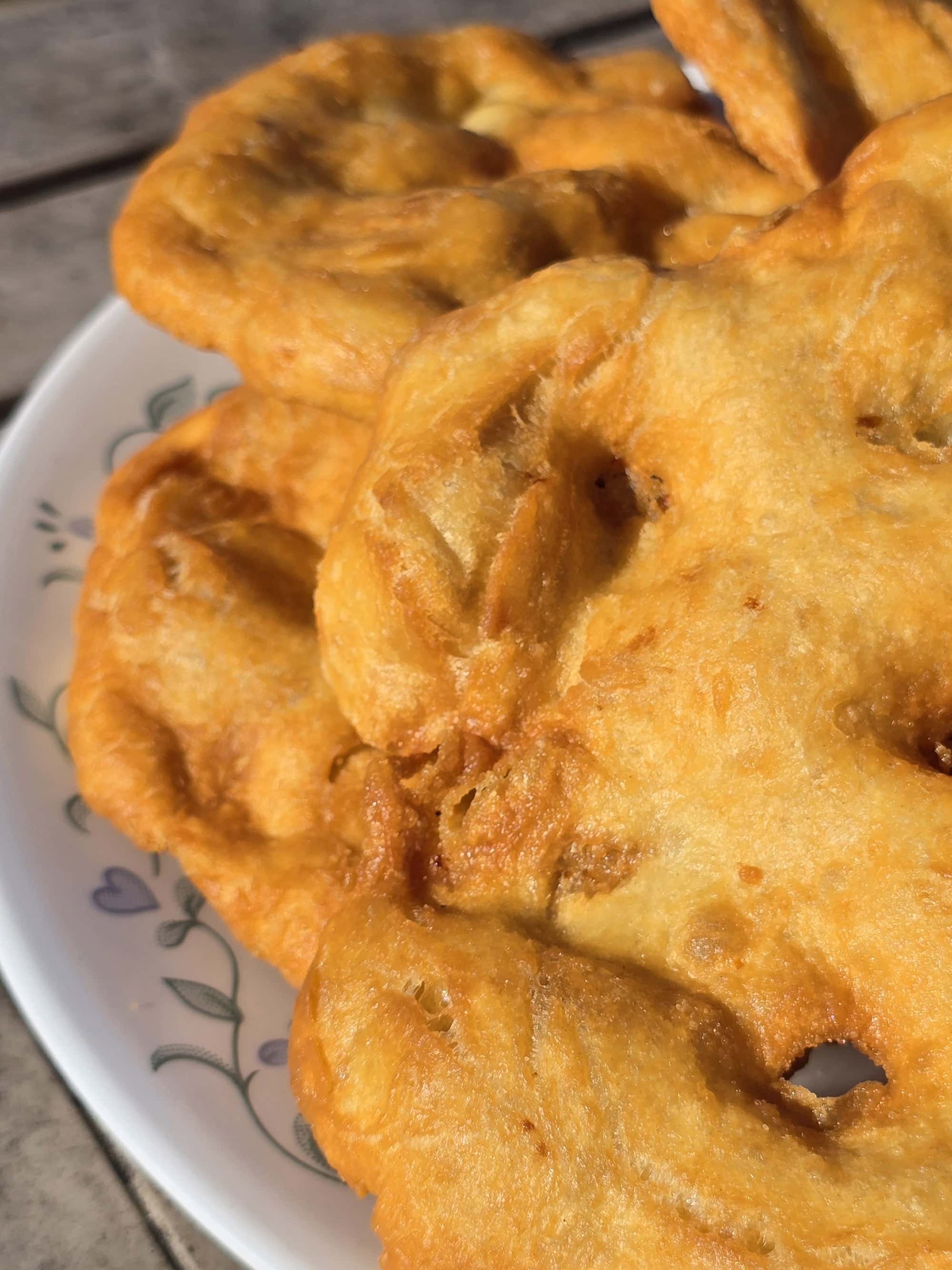 3 large pieces of homemade Fry bread on a plate, on a wooden dock.