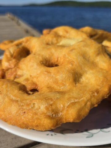 3 large pieces of Indian Fry bread on a plate, on a wooden dock.