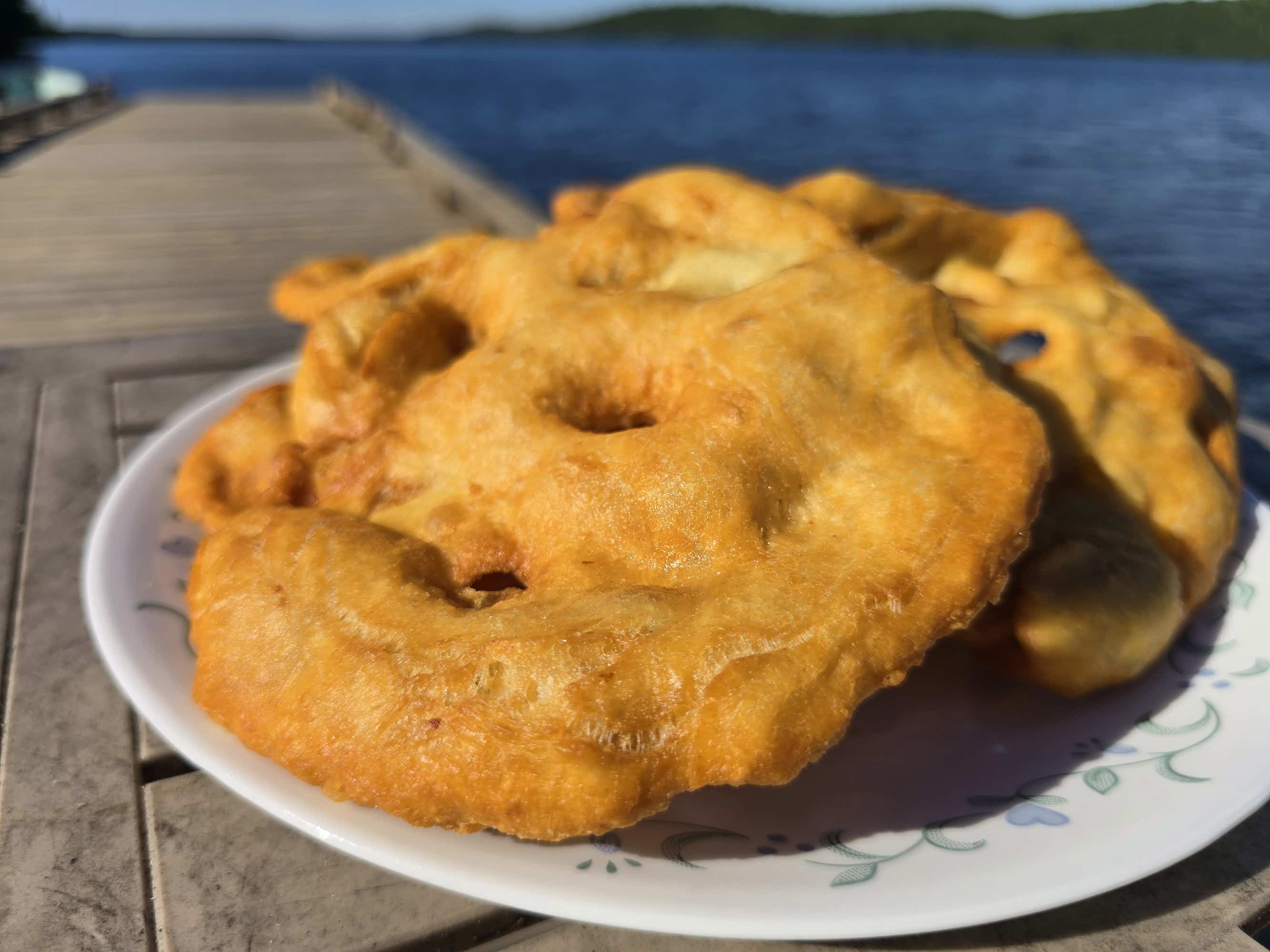3 large pieces of Indian Fry bread on a plate, on a wooden dock.