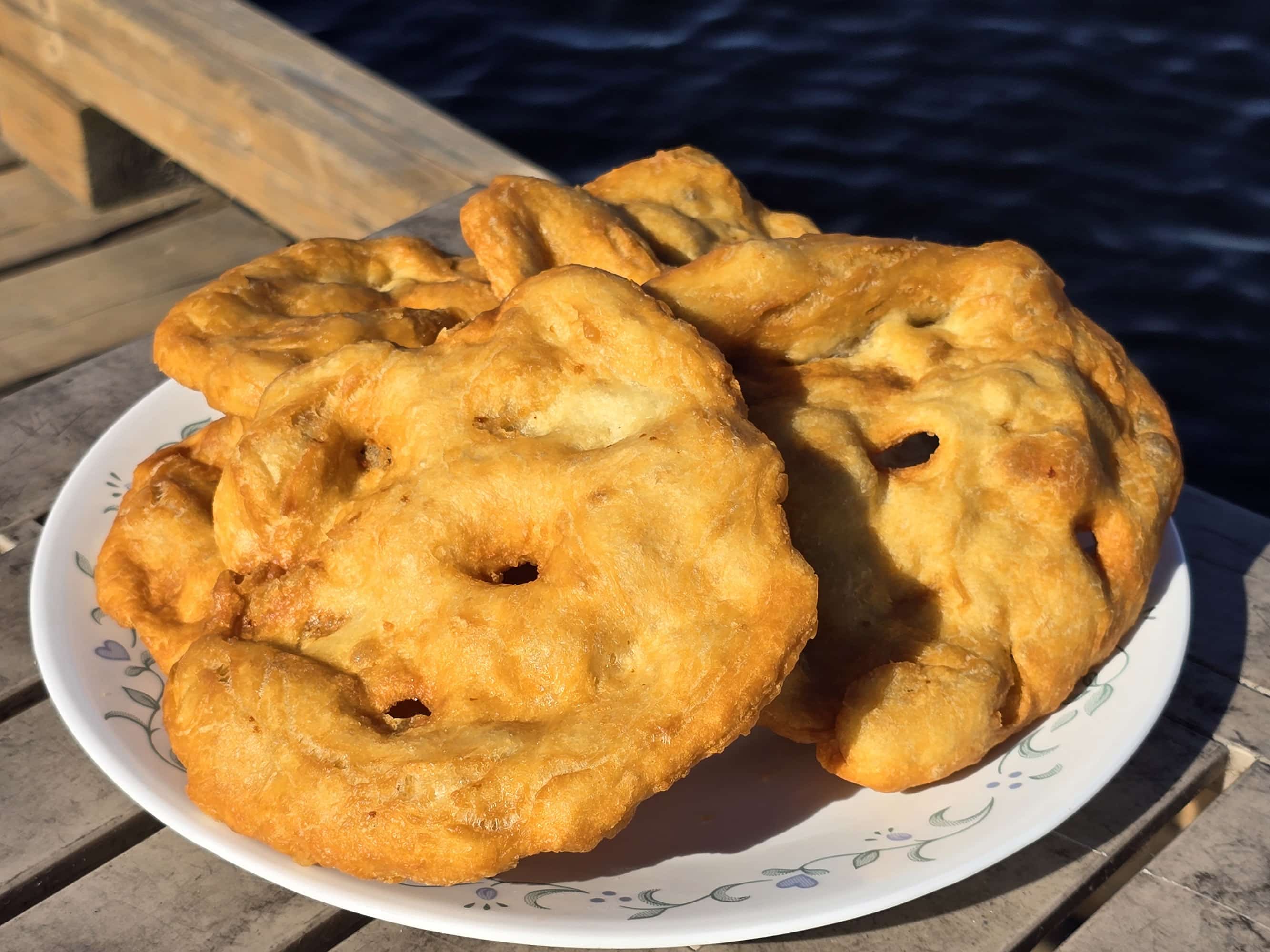 3 large pieces of homemade Frybread on a plate, on a wooden dock.