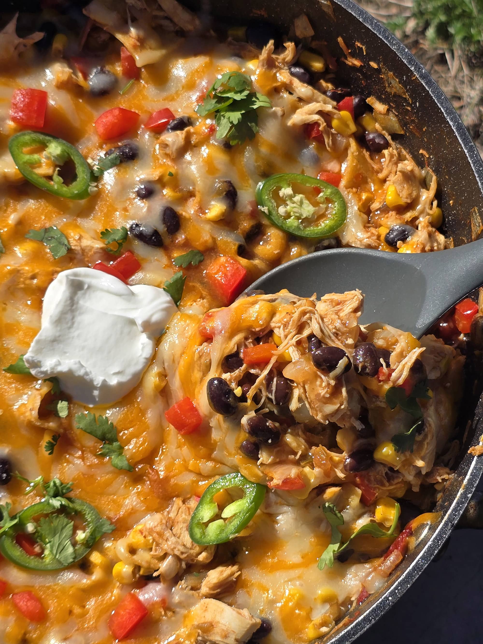 A pan of deconstructed enchilada skillet - red peppers, onions, corn, black beans, chicken, and enchilada sauce with cheese.