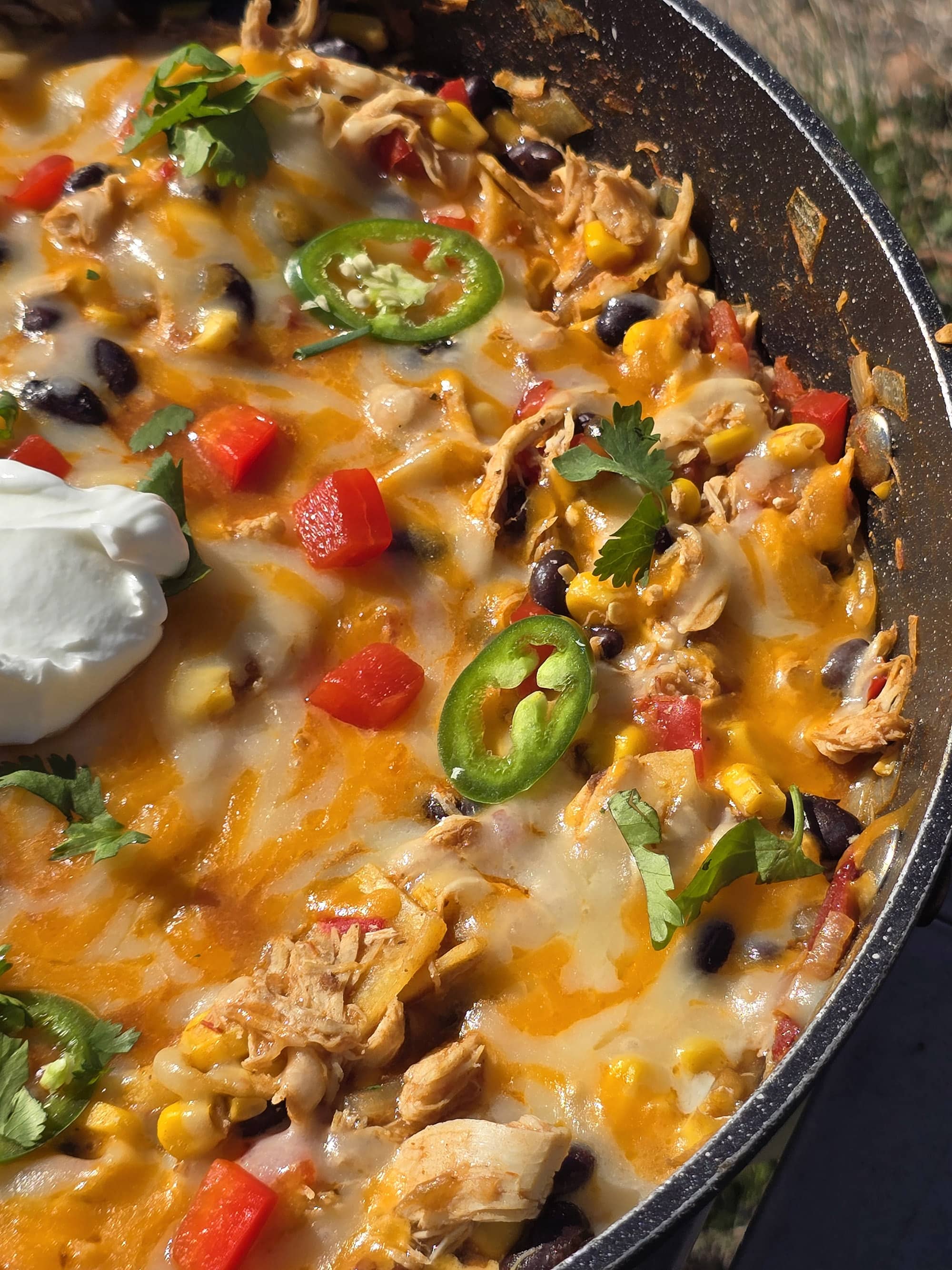 A pan of deconstructed enchilada skillet - red peppers, onions, corn, black beans, chicken, and enchilada sauce with cheese.