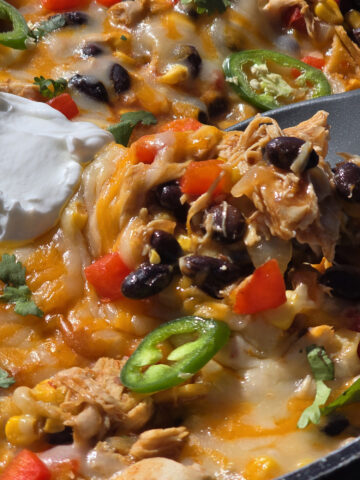 A pan of deconstructed enchilada skillet - red peppers, onions, corn, black beans, chicken, and enchilada sauce with cheese.