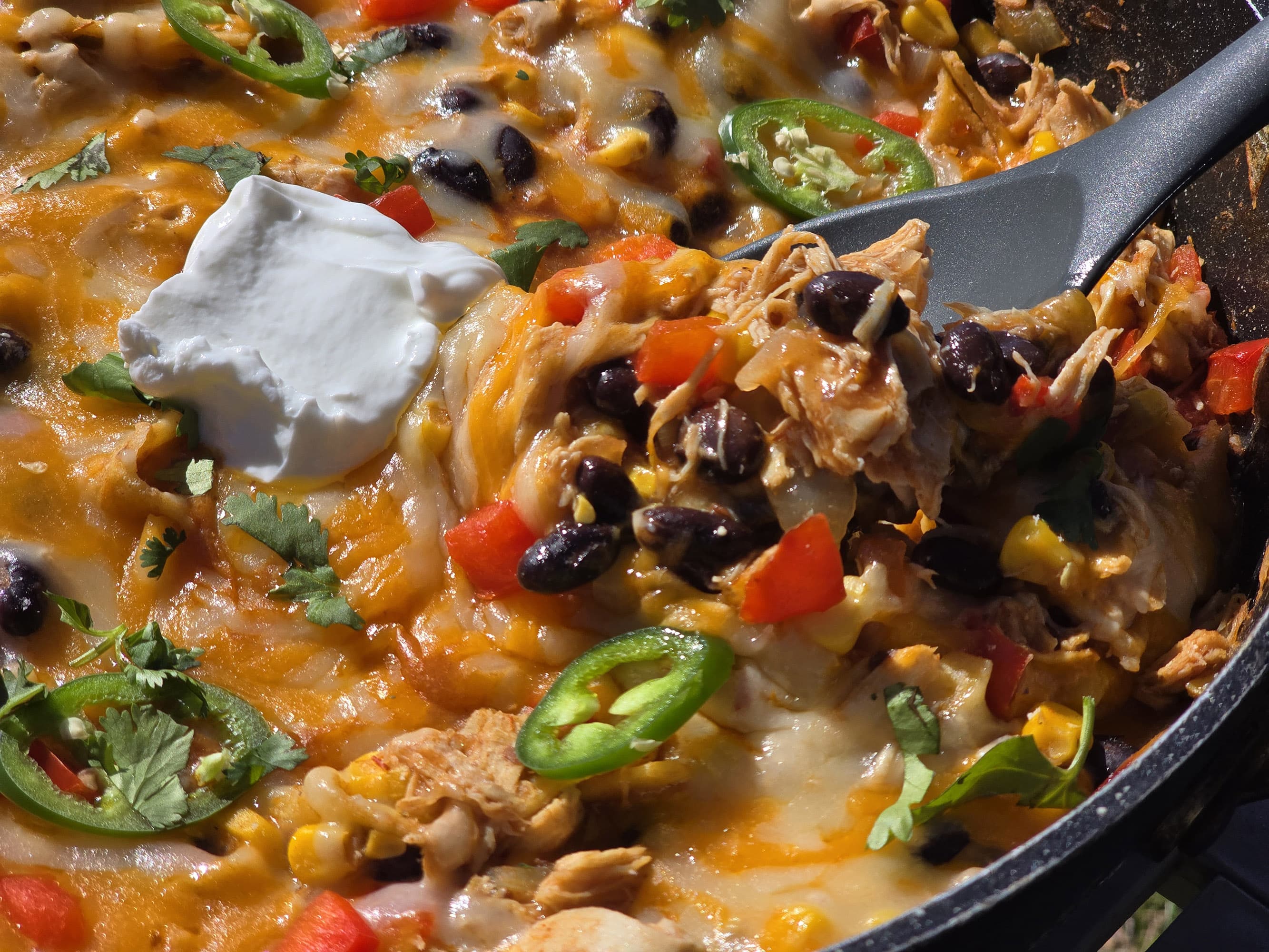 A pan of deconstructed enchilada skillet - red peppers, onions, corn, black beans, chicken, and enchilada sauce with cheese.
