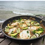 A pan of Huevos Enfrijolados, garnished with lime slices, avocado, cilantro, and crumbled queso fresco.