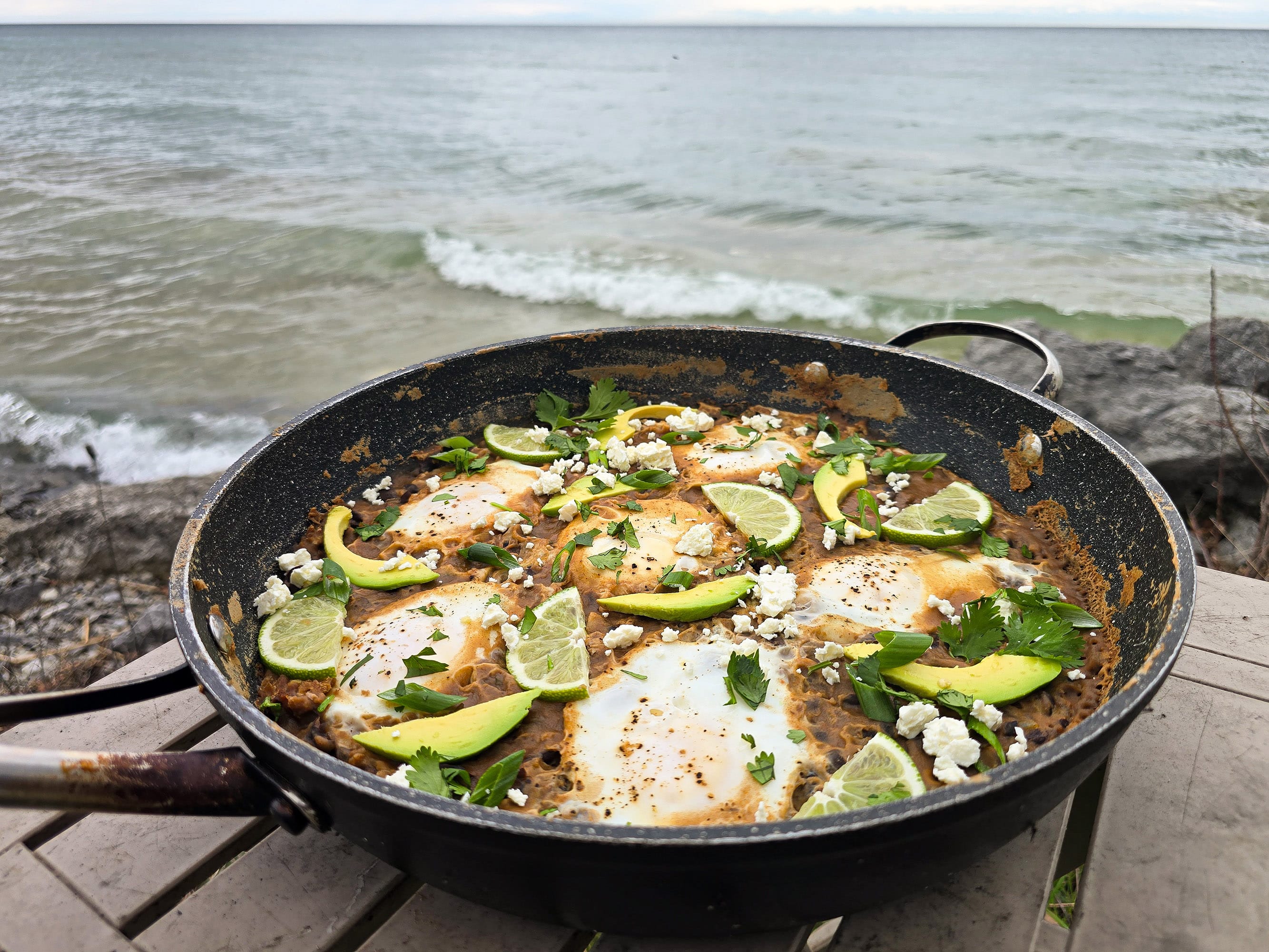 A pan of Huevos Enfrijolados, garnished with lime slices, avocado, cilantro, and crumbled queso fresco.