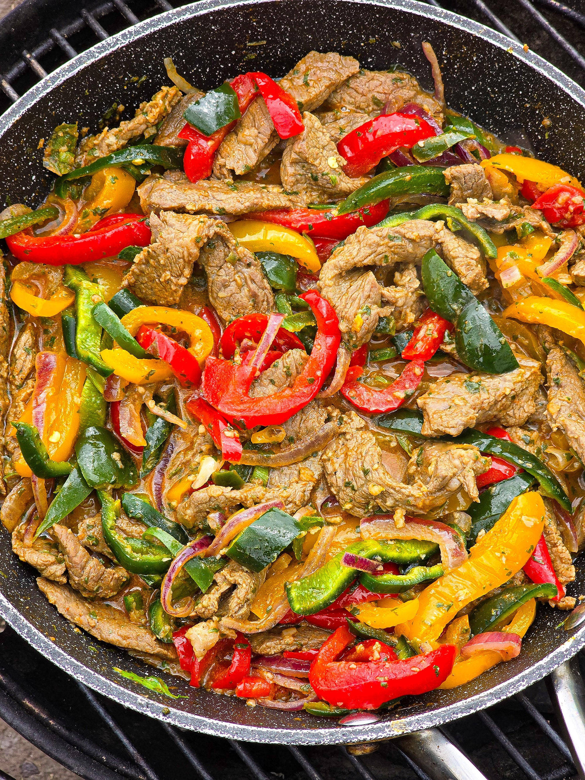 Steak Fajitas filling with marinated beef strips, multicoloured bell peppers, poblano peppers, and jalapeno in a skillet.