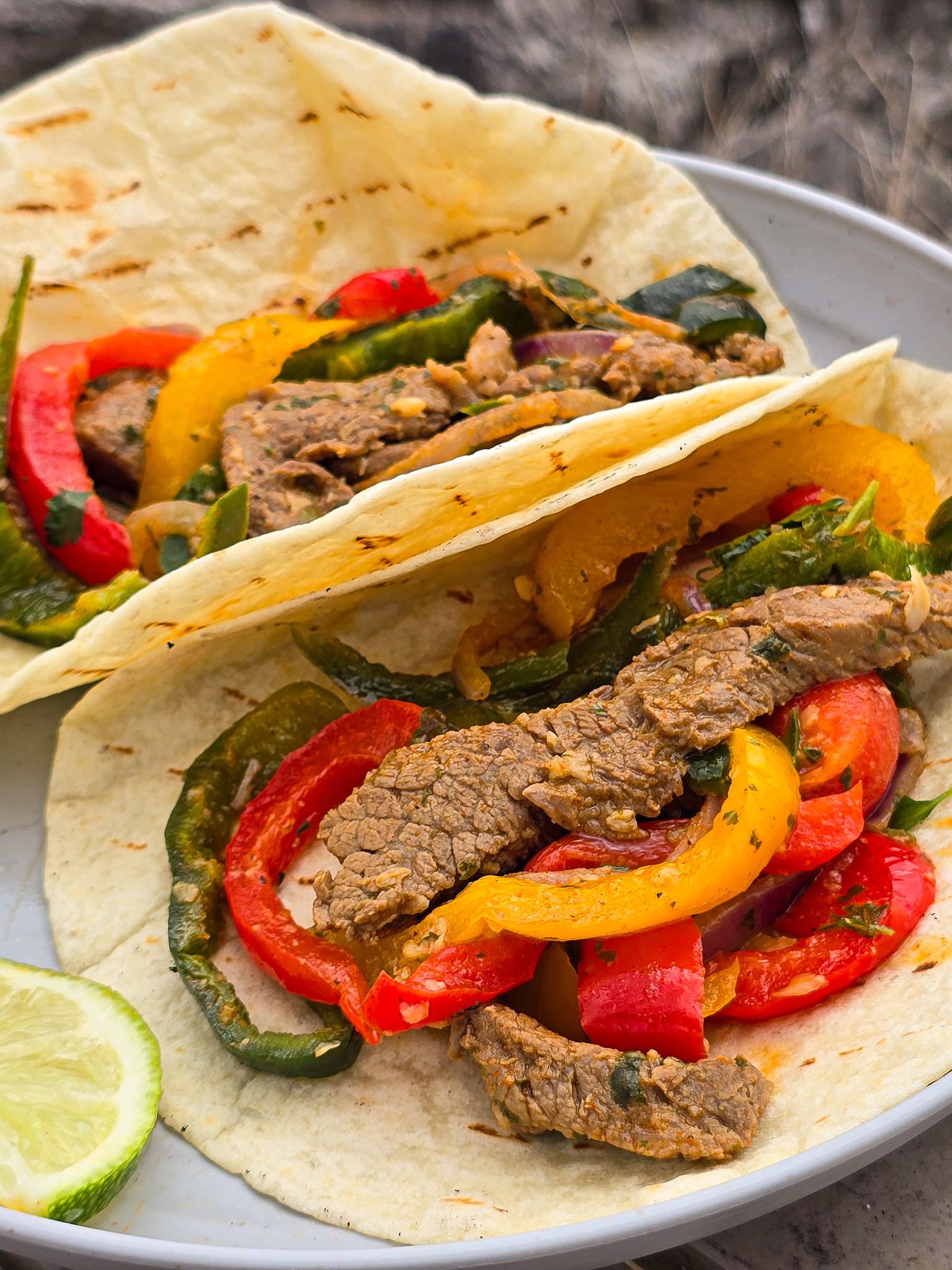 2 skillet pepper and steak fajitas on a plate with sour cream and a slice of lime.