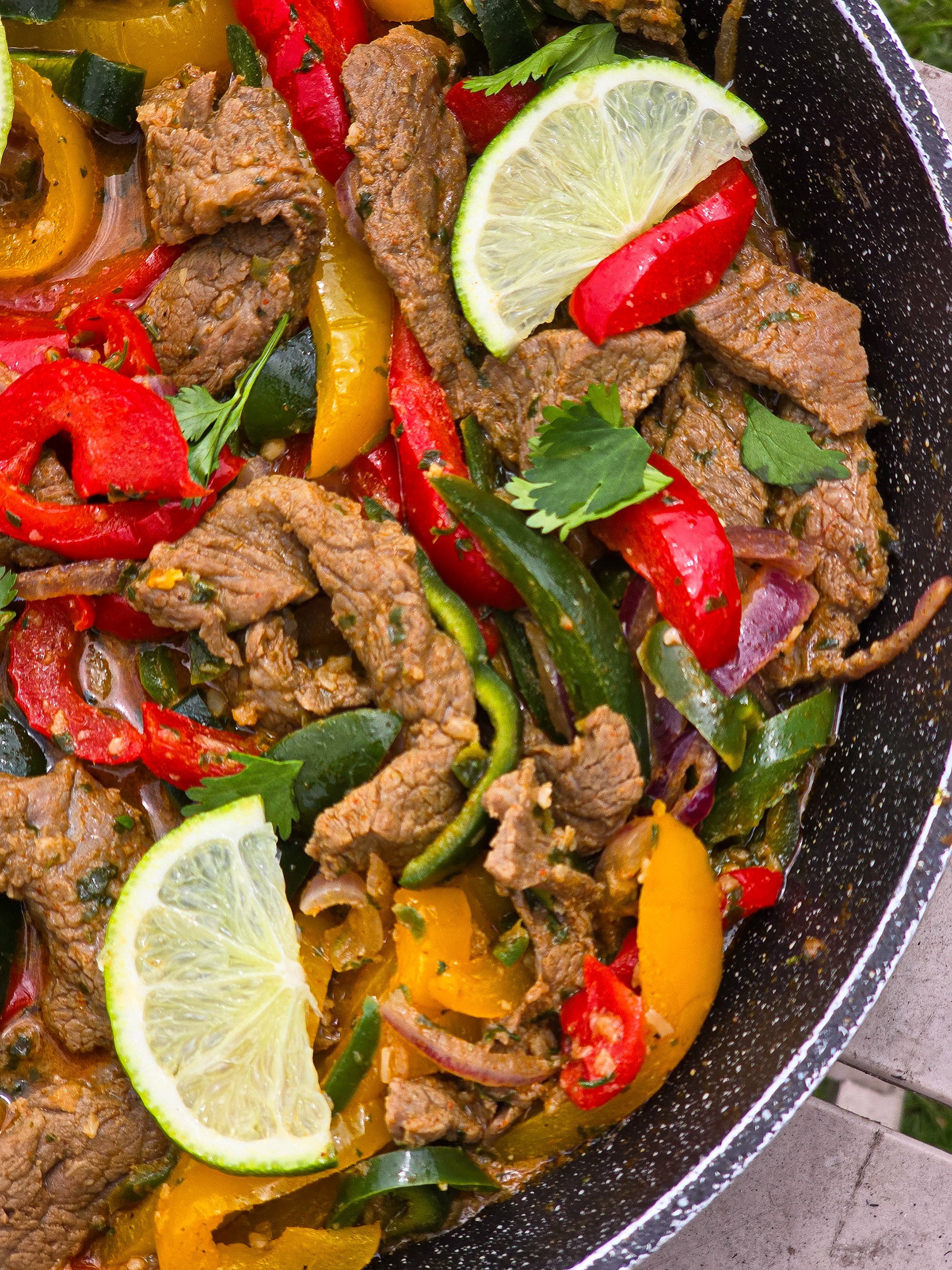 Beef Fajitas filling with marinated steak strips, multicoloured bell peppers, poblano peppers, and jalapeno in a skillet.