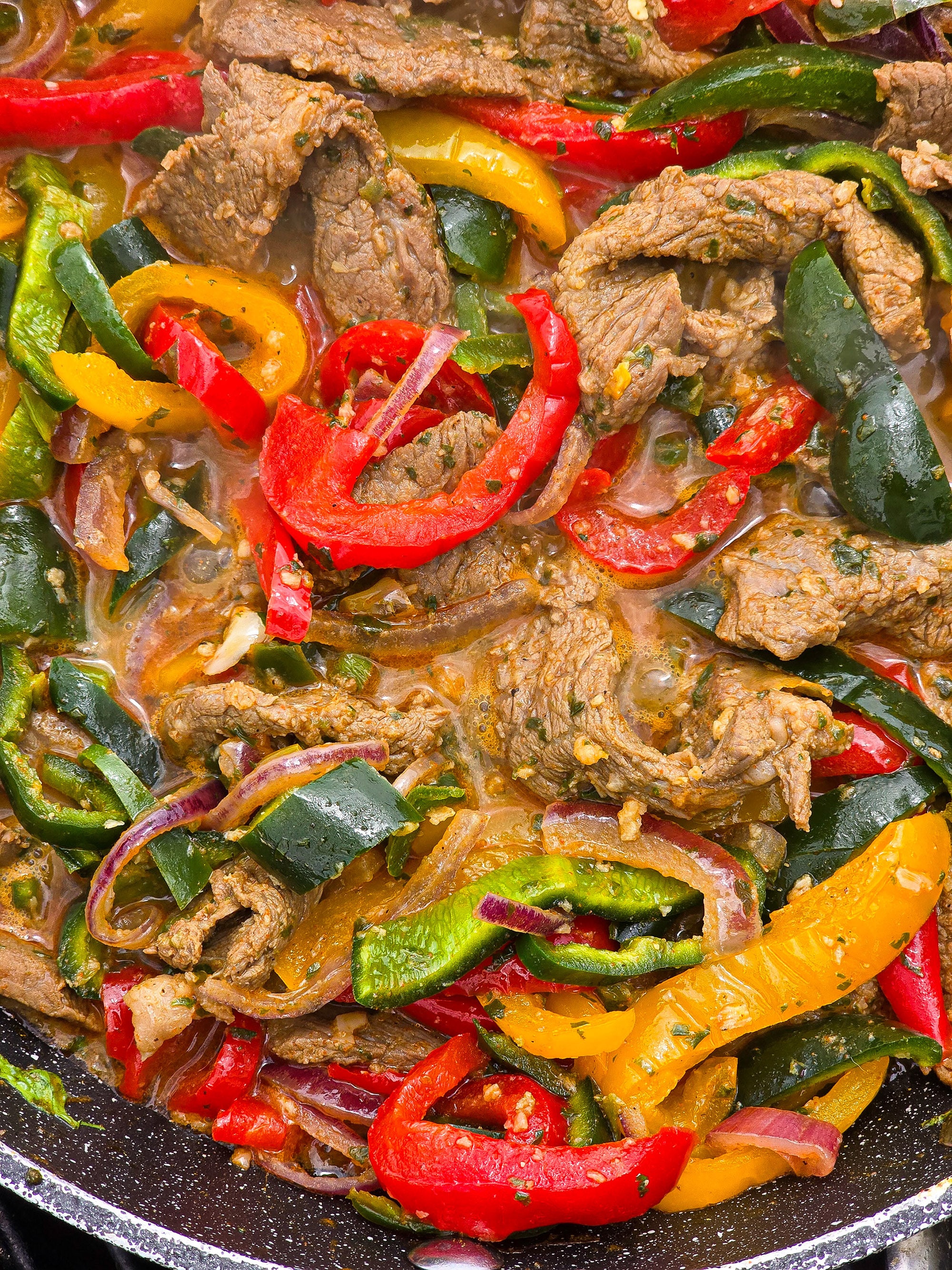 Steak Fajita filling with marinated beef strips, multicoloured bell peppers, poblano peppers, and jalapeno in a skillet.