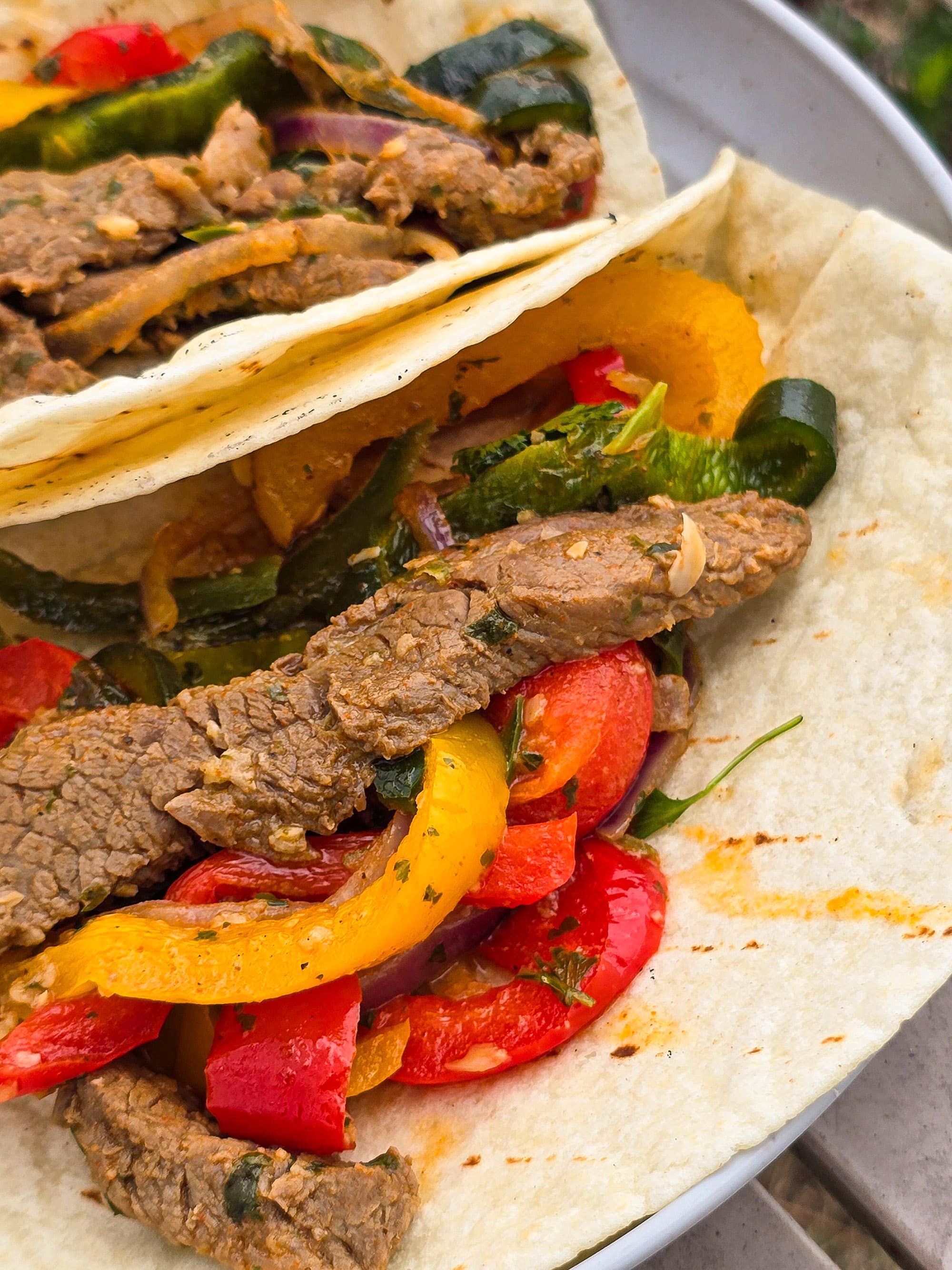 2 skillet pepper and steak fajitas on a plate with sour cream and a slice of lime.
